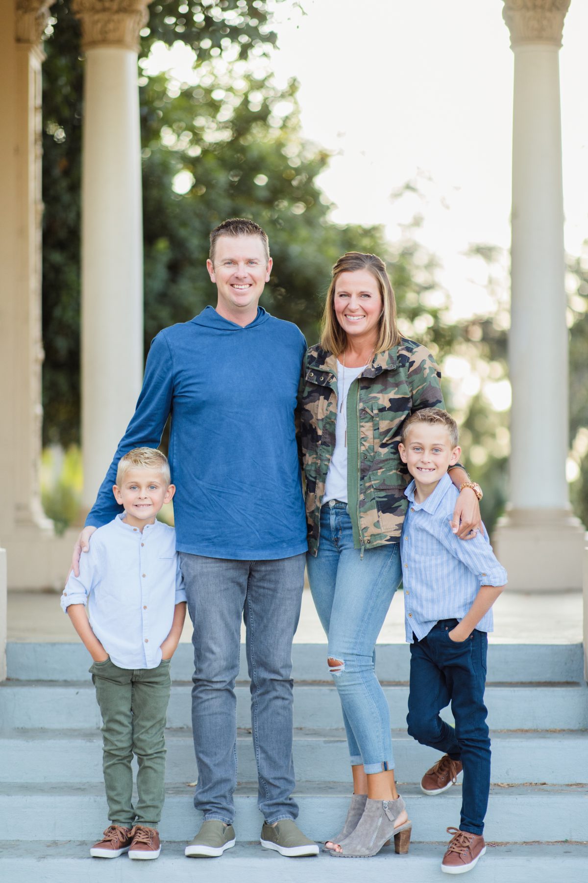Family of four poses on stone steps beside classic columns