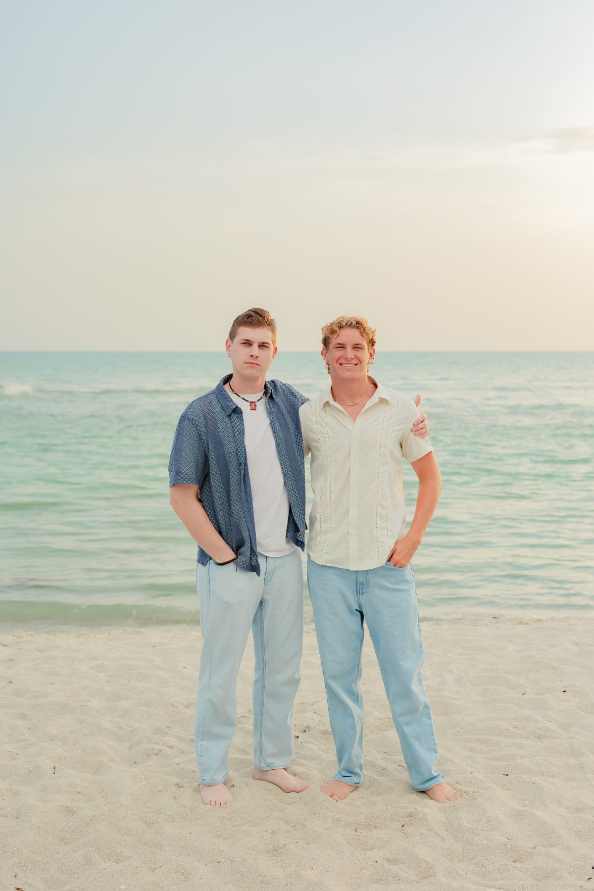 Two young men in beach attire stand side by side on the shore