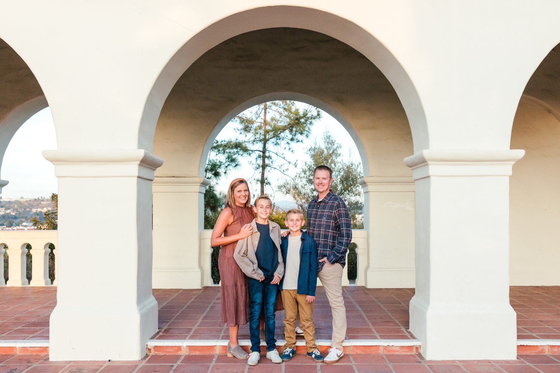 Family of four poses under mission-style arches, San Diego family photographer session