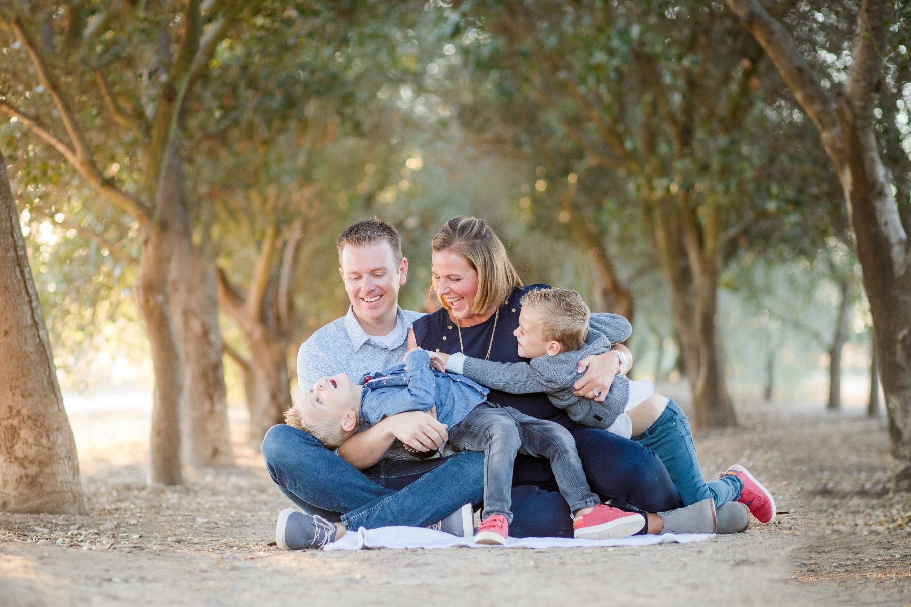 Parents laugh while hugging two boys seated on a sandy trail