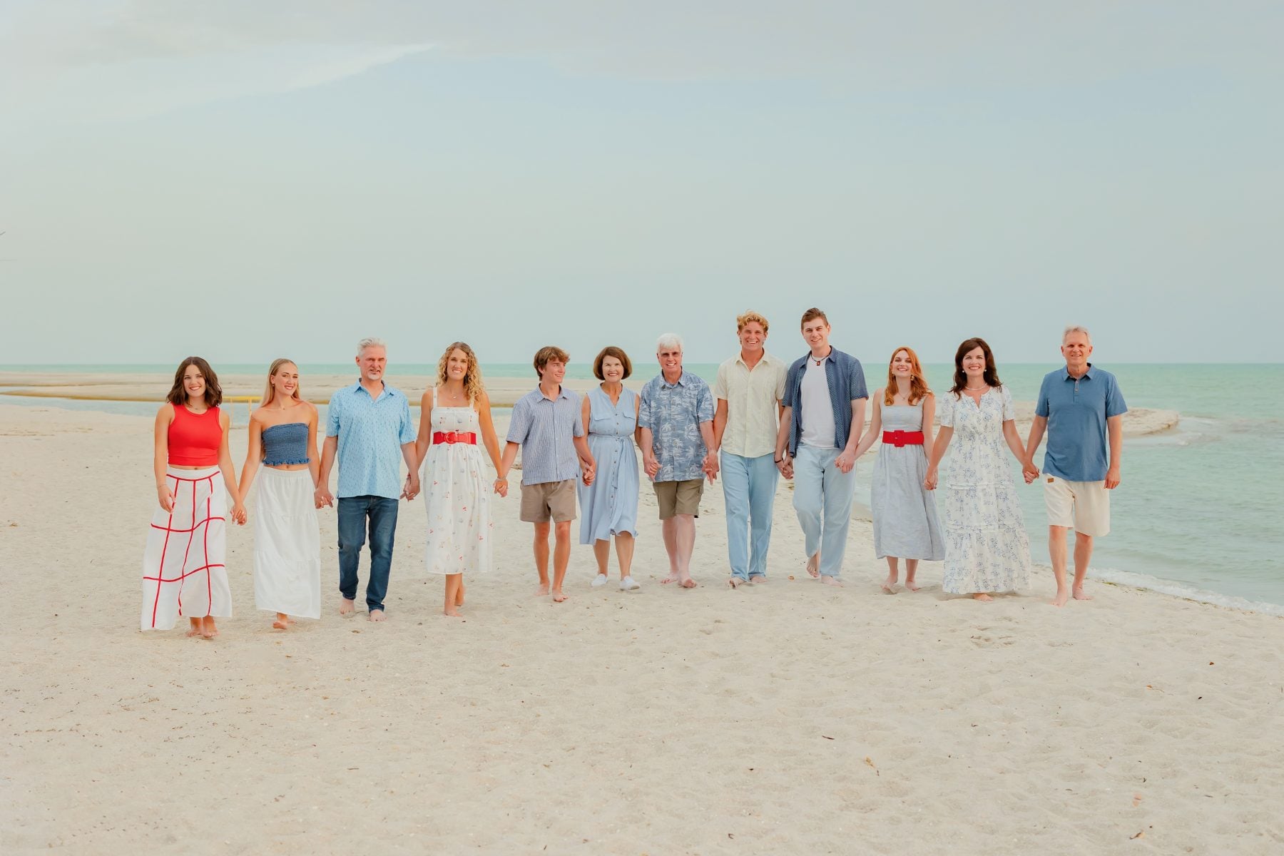 Extended family holds hands walking along Captiva Island beach at sunset
