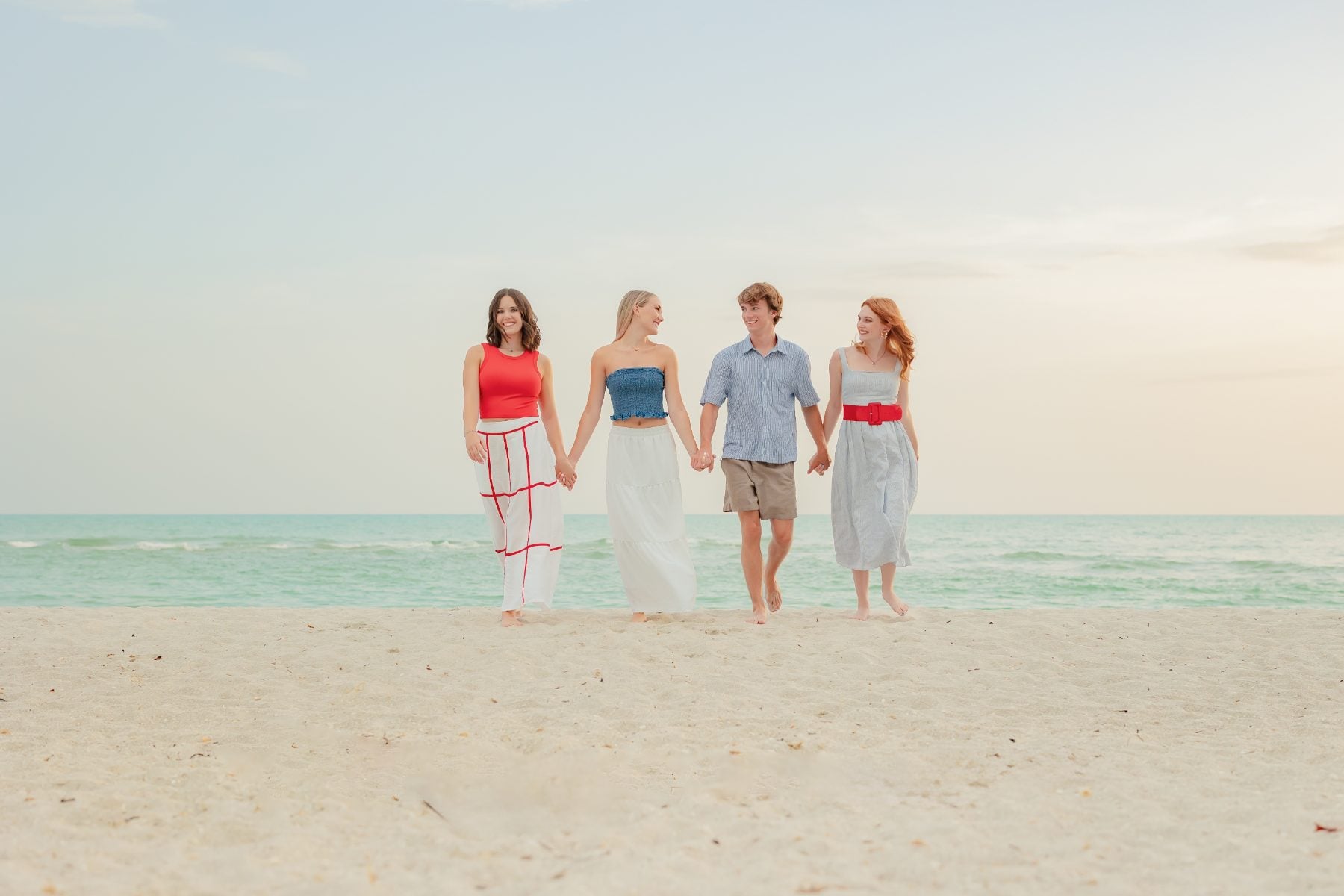 Four siblings walk hand in hand along the shoreline
