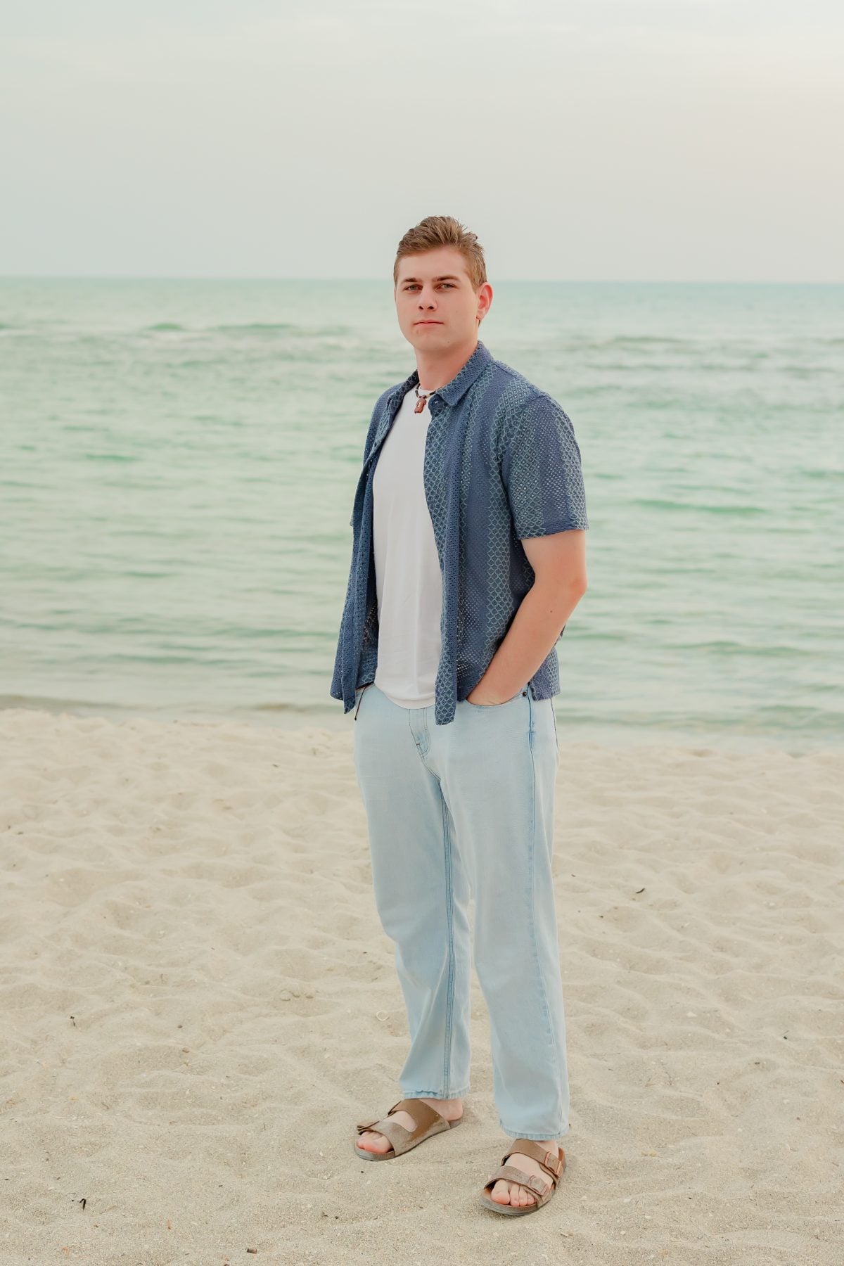 Young man in blue shirt stands confidently on the beach