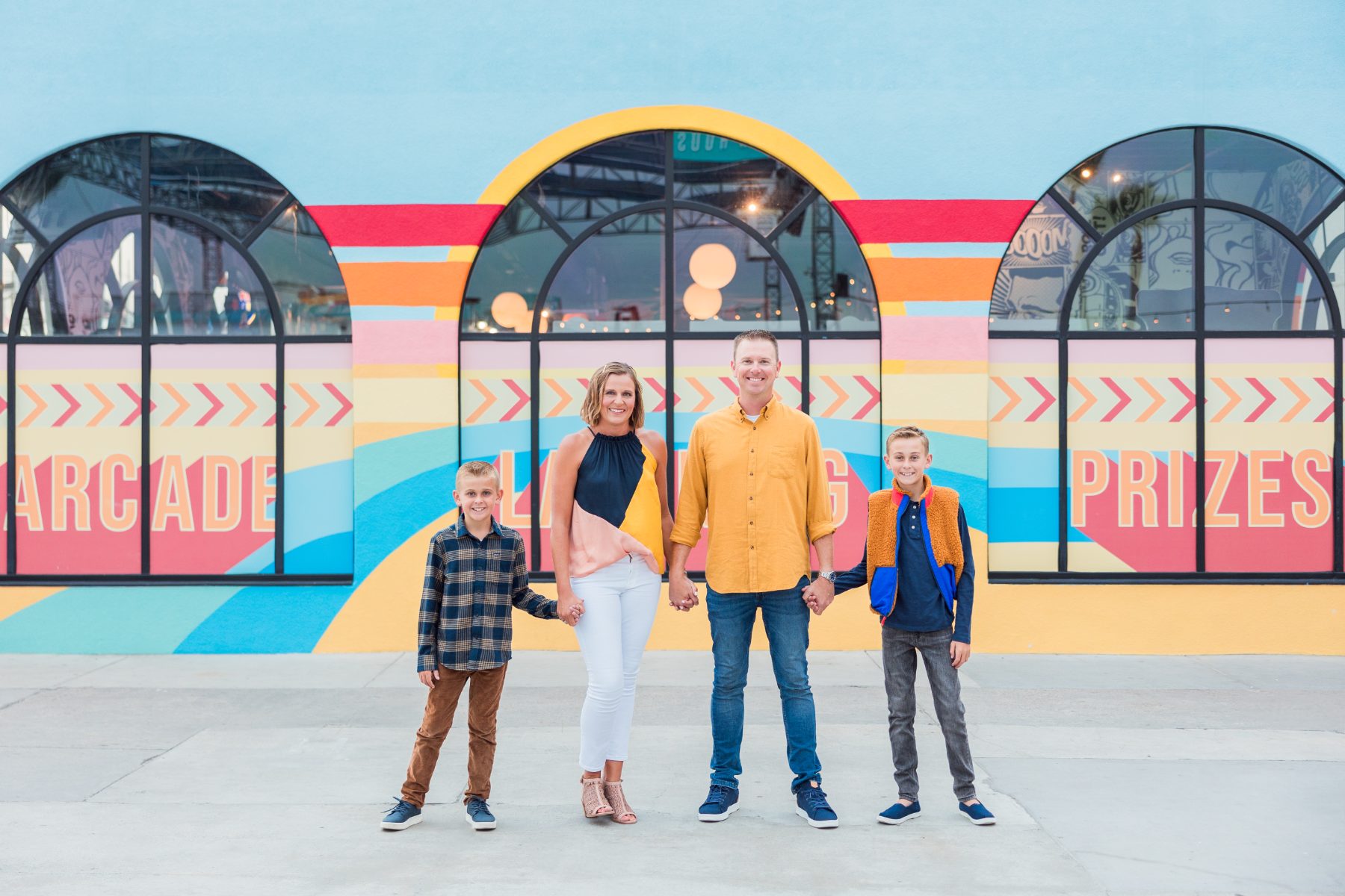 Family of four holds hands before a colorful arcade mural wall