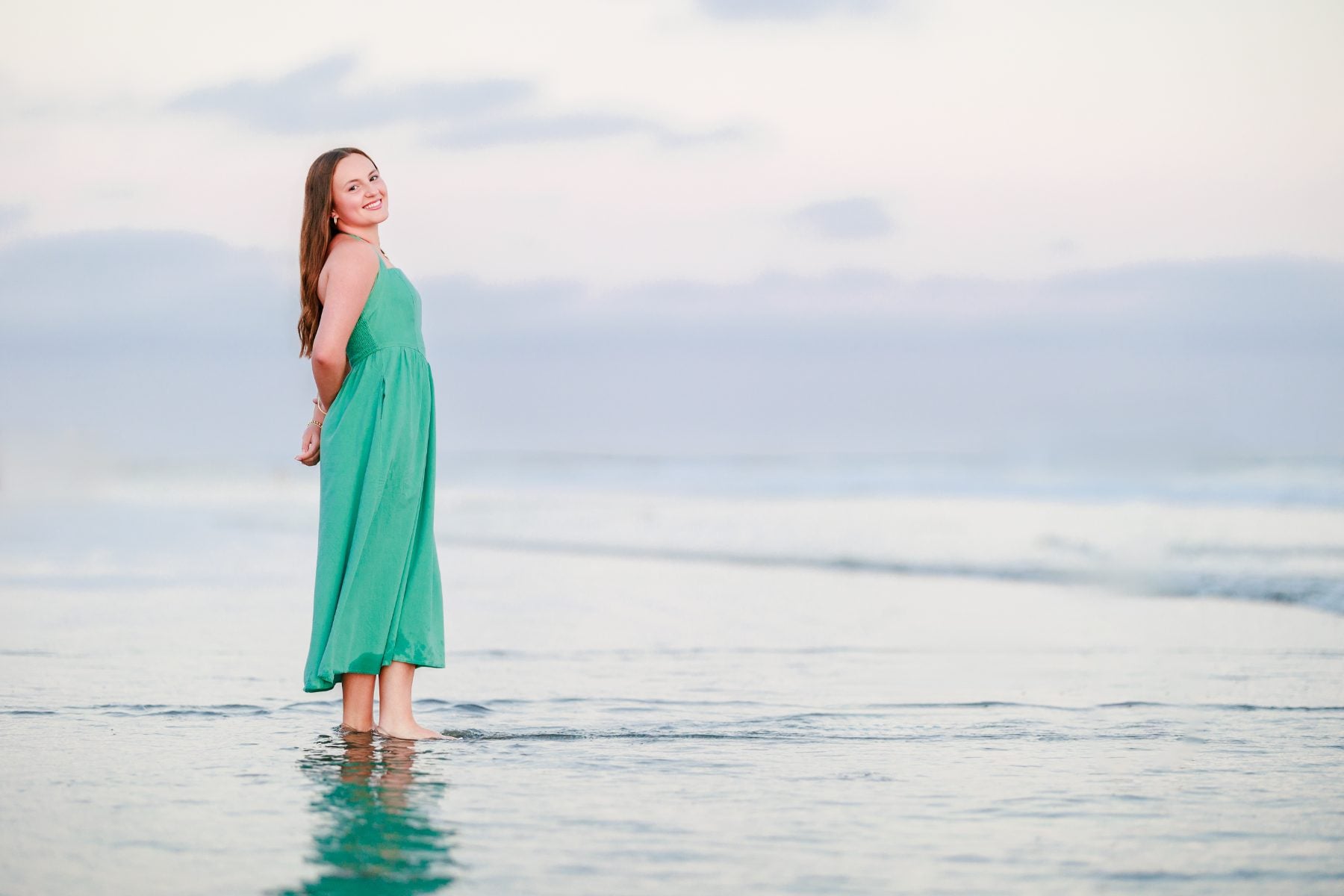 Woman in green dress wades in shallow water at Coronado Beach