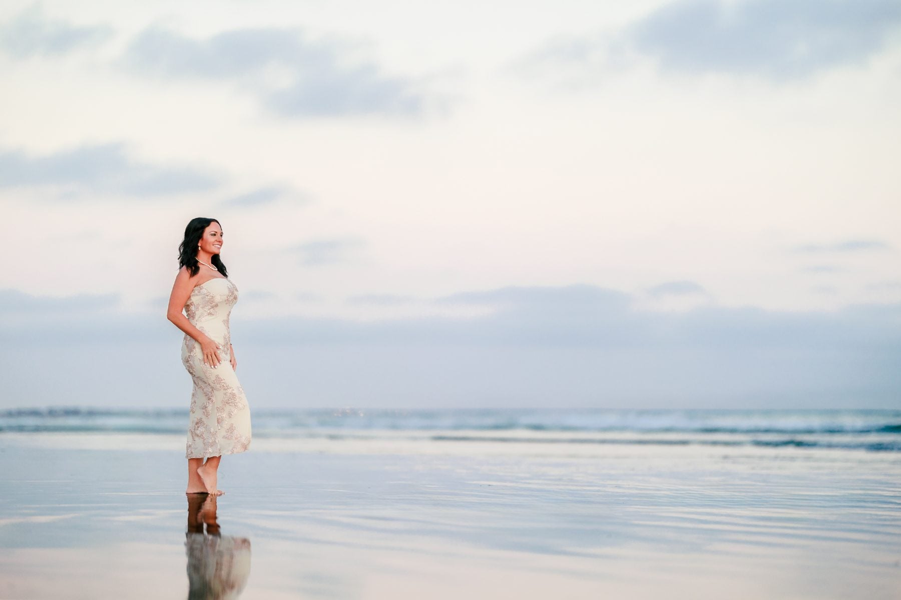 Woman in white dress stands alone on Coronado Beach at sunset