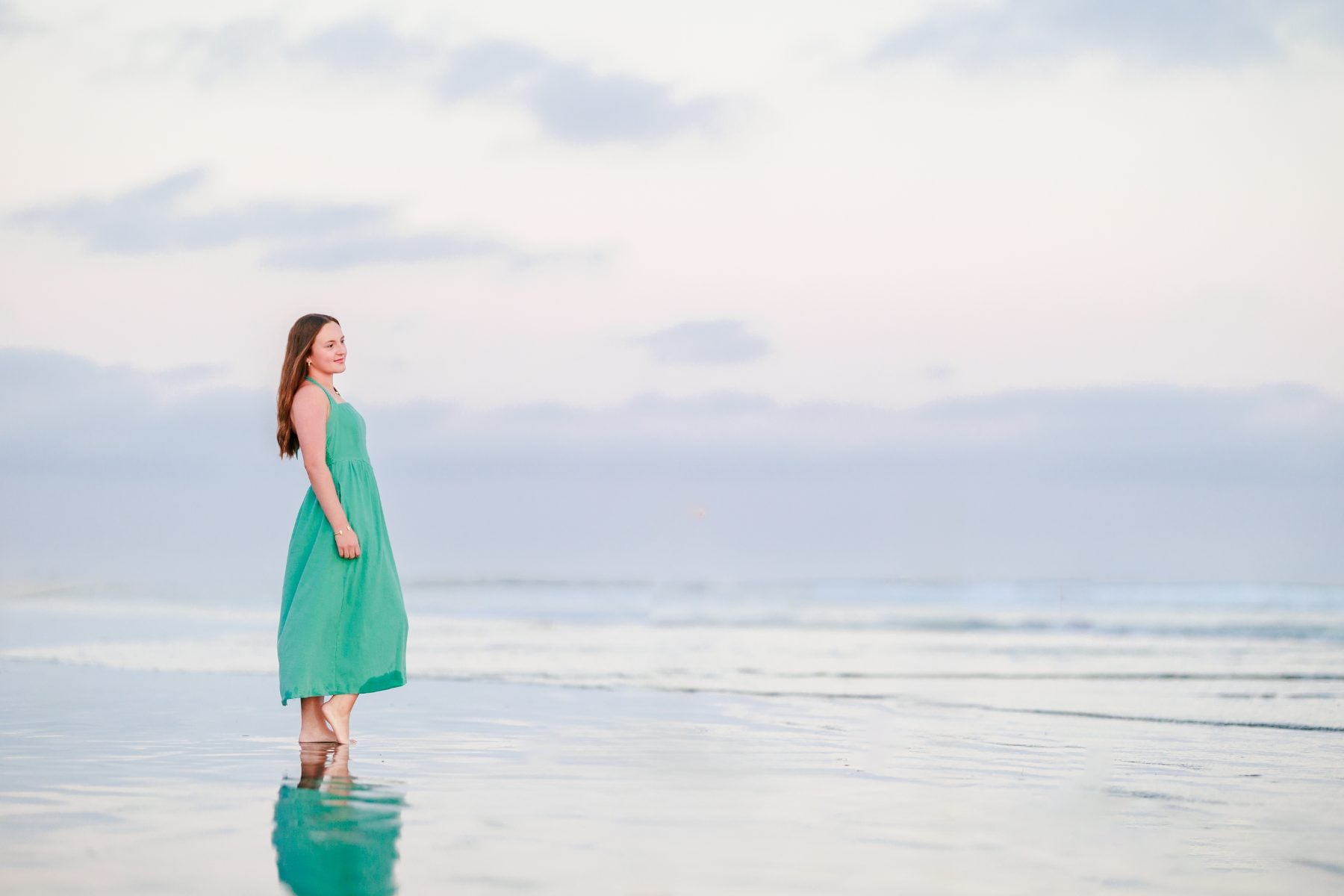 Woman in teal dress glances back while standing on Coronado Beach