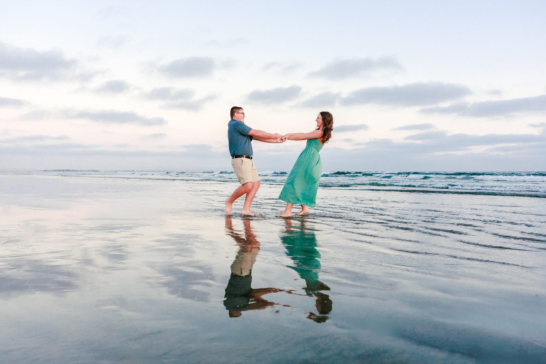 Couple holds hands dancing on Coronado Beach at sunset with reflections