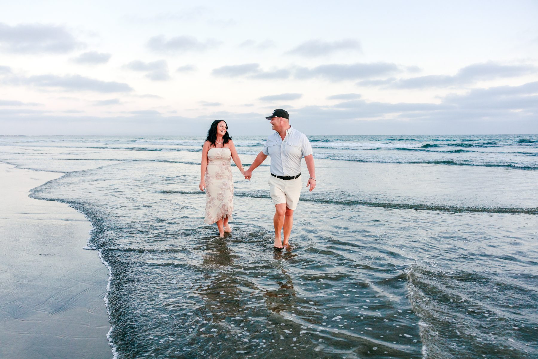 Couple holds hands walking through shallow surf at Coronado Beach