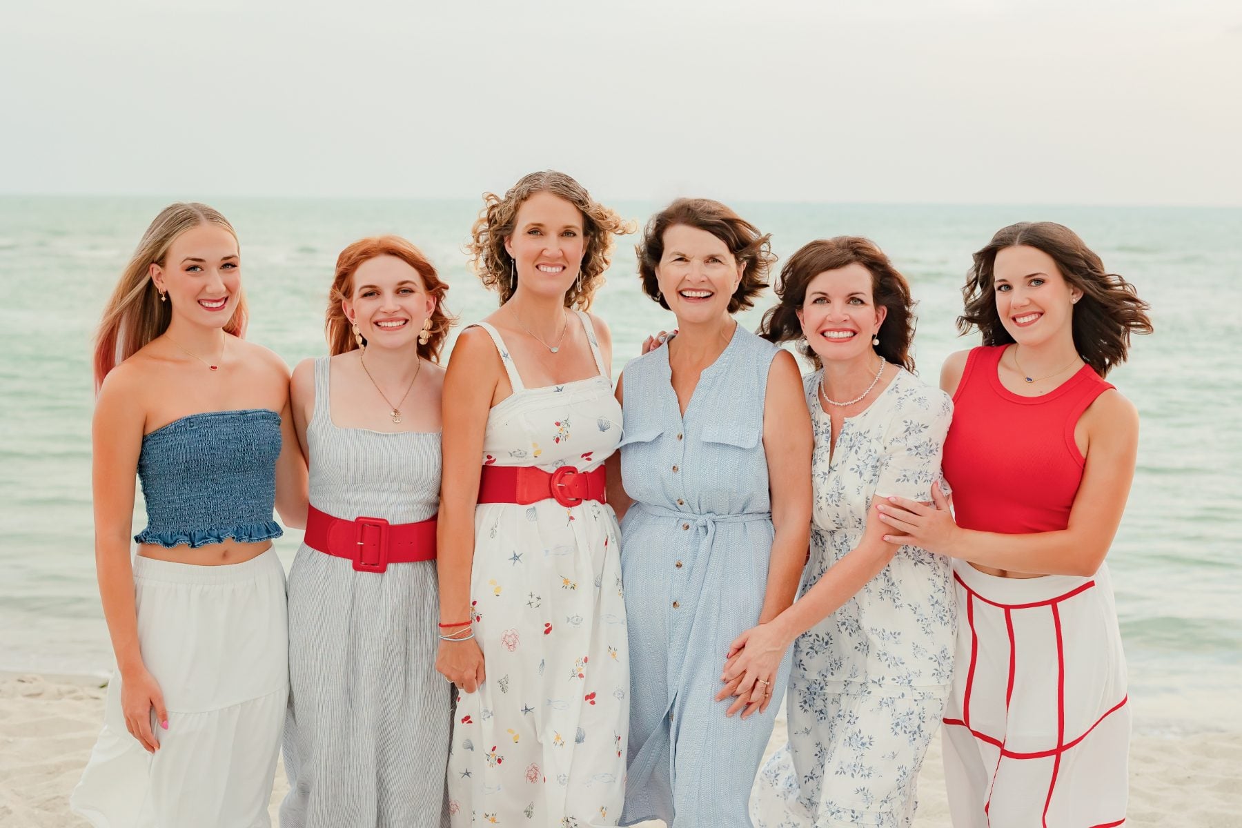 Extended family of six women smiling for a group beach portrait