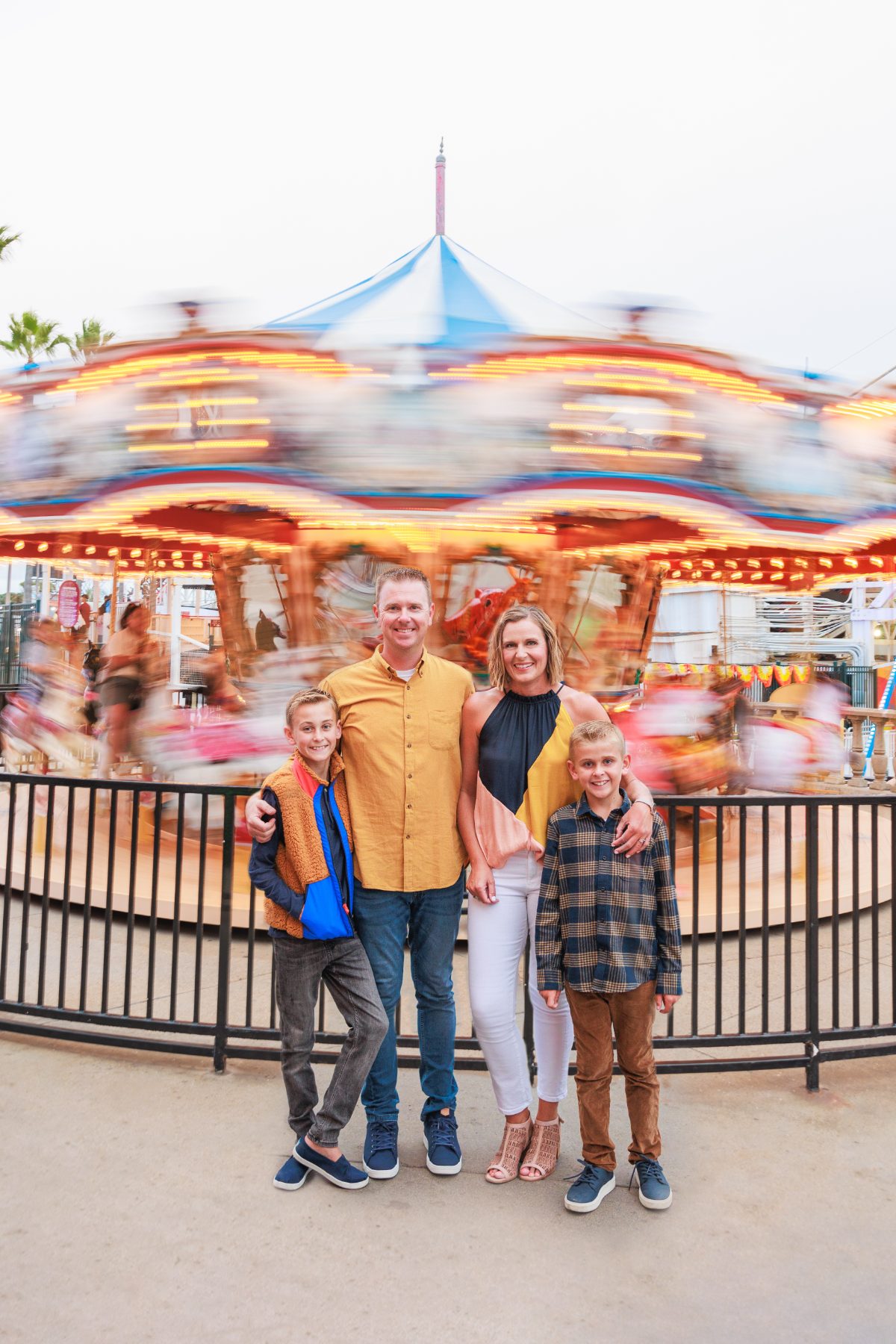 Family standing near a spinning, light-blur carousel at an evening fair