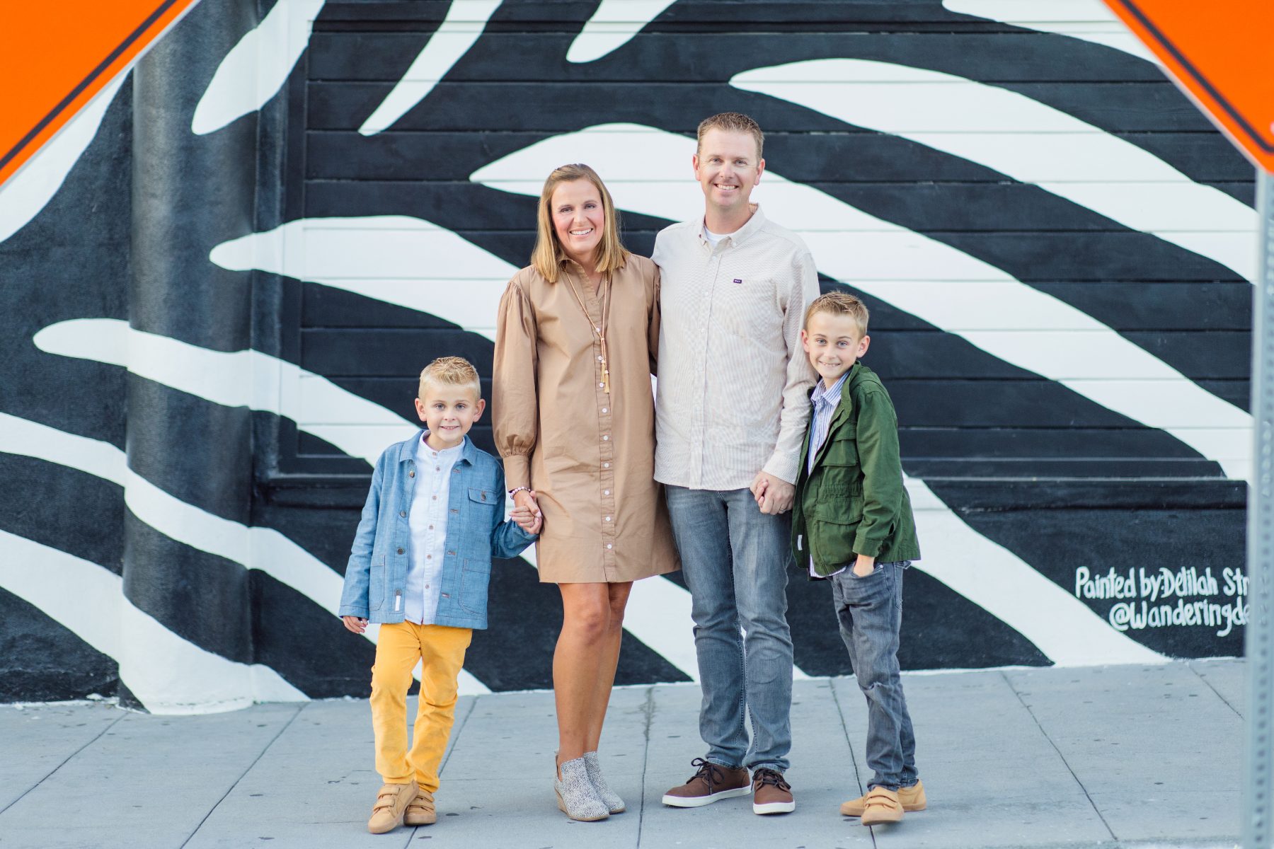 Family of four holding hands in front of a black and white zebra mural