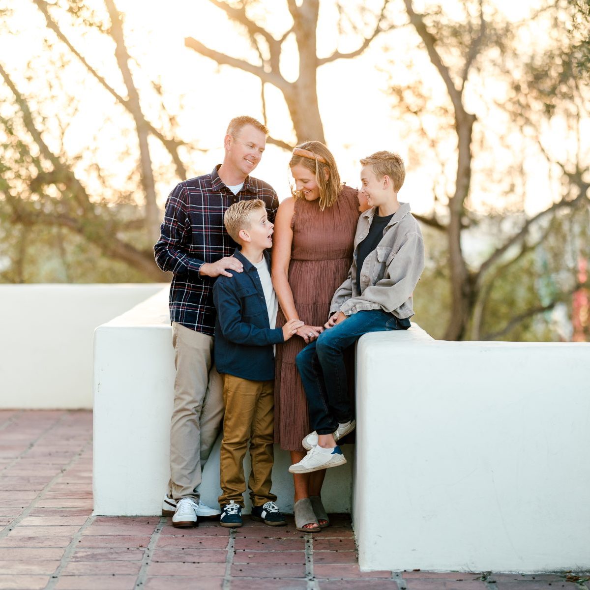 Family gathered close around white concrete benches under trees at golden hour