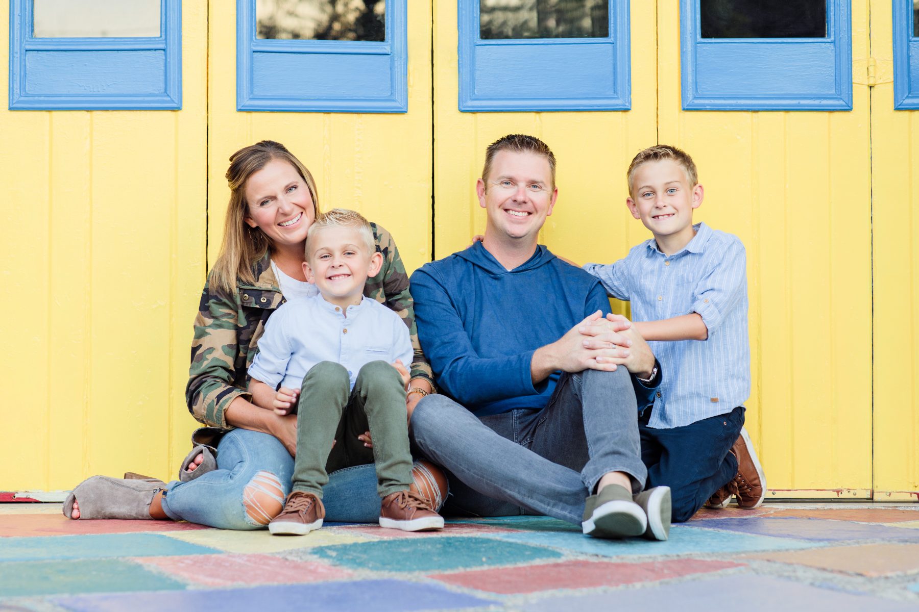 Parents and two boys sitting in front of a bright yellow building with blue shutters