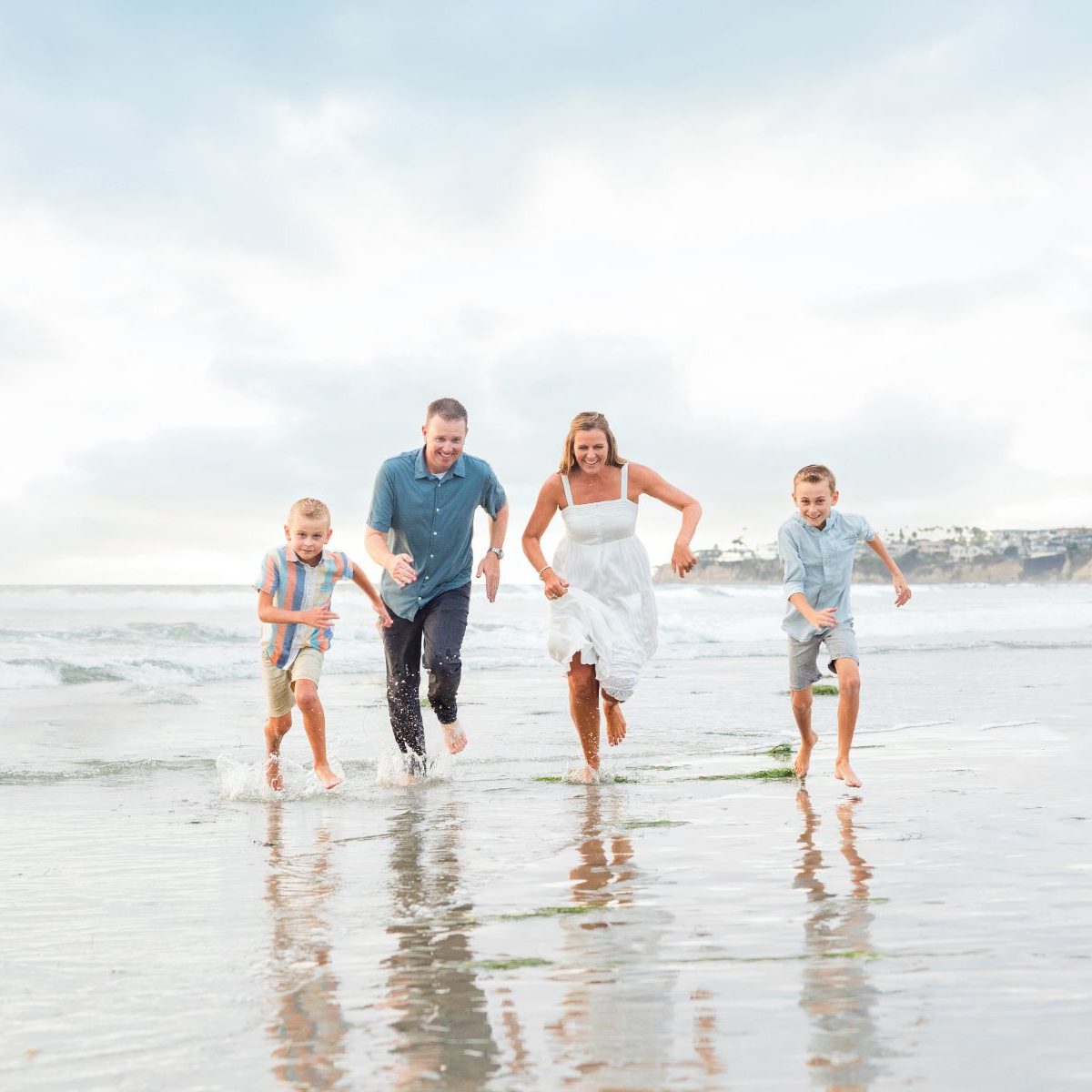 Parents and two boys run laughing through the surf at the beach