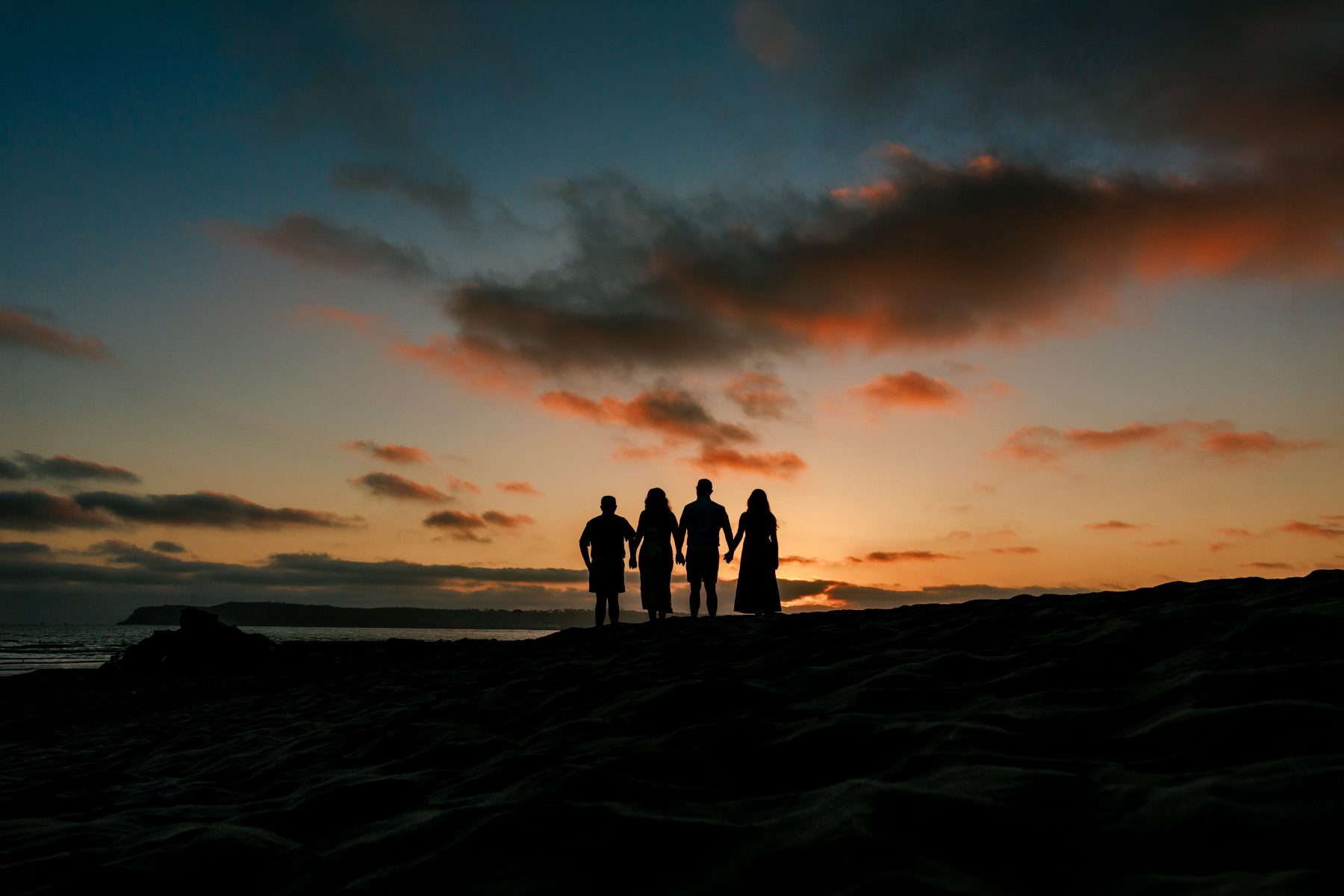 Silhouette of family of four holding hands at sunset on beach