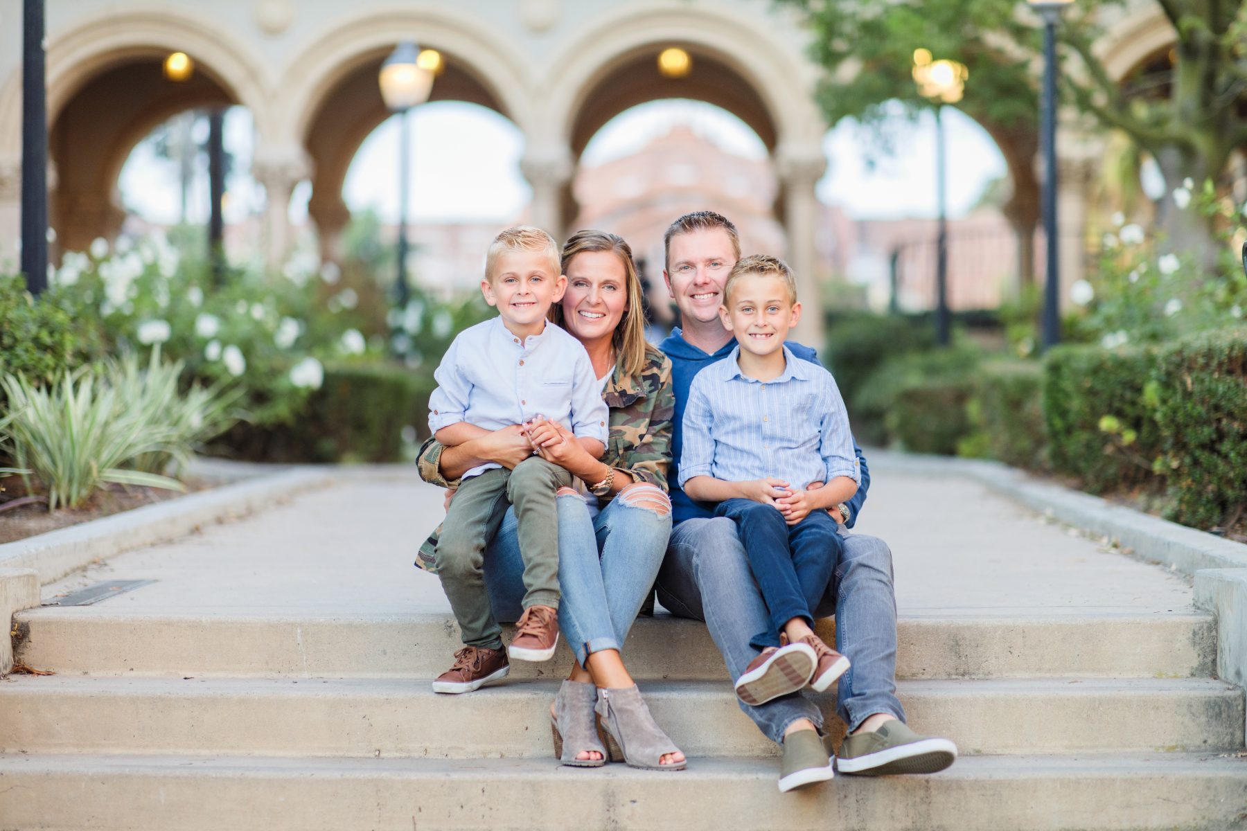 Family of four sitting together on stone steps beside an arched courtyard