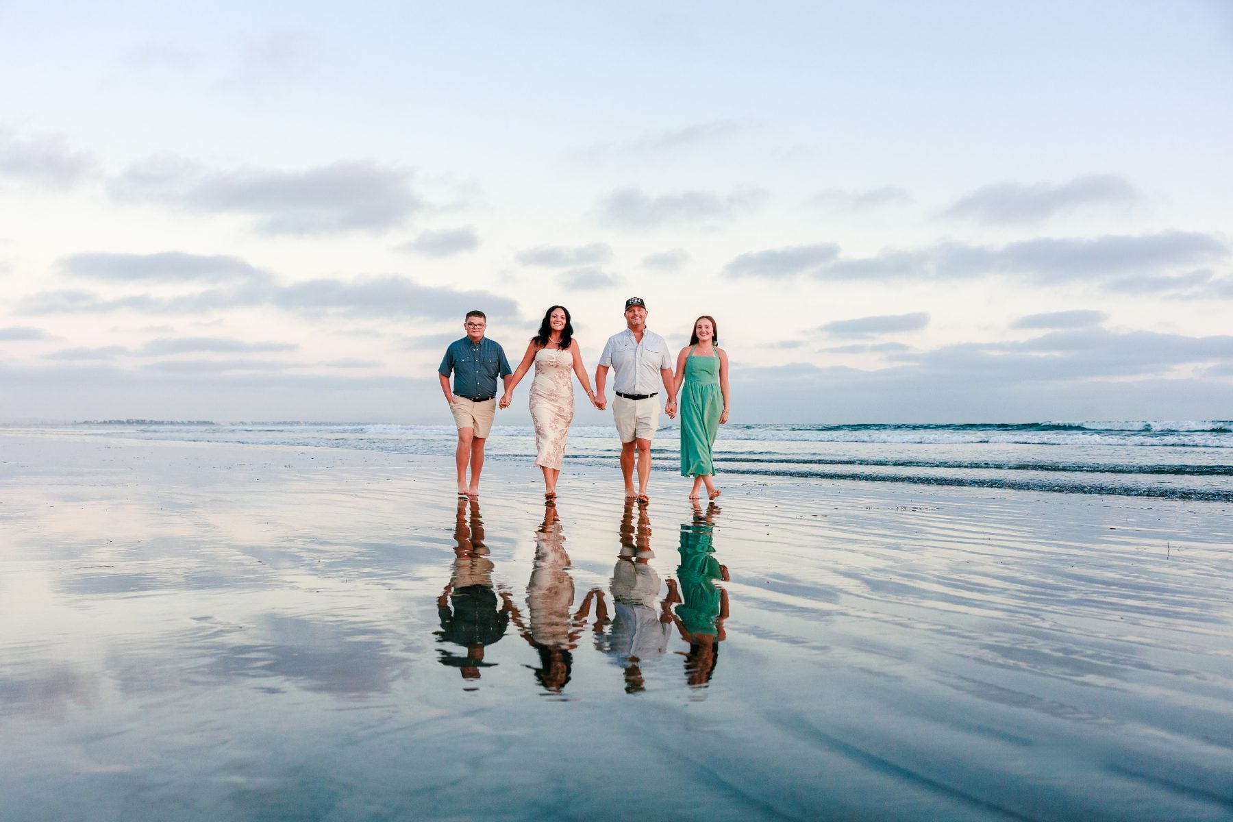 Family of four walks hand in hand along Coronado Beach shoreline