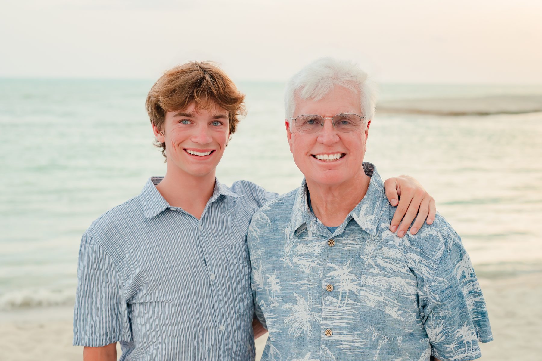 Father and son in blue shirts embrace on Sanibel Island beach at sunset