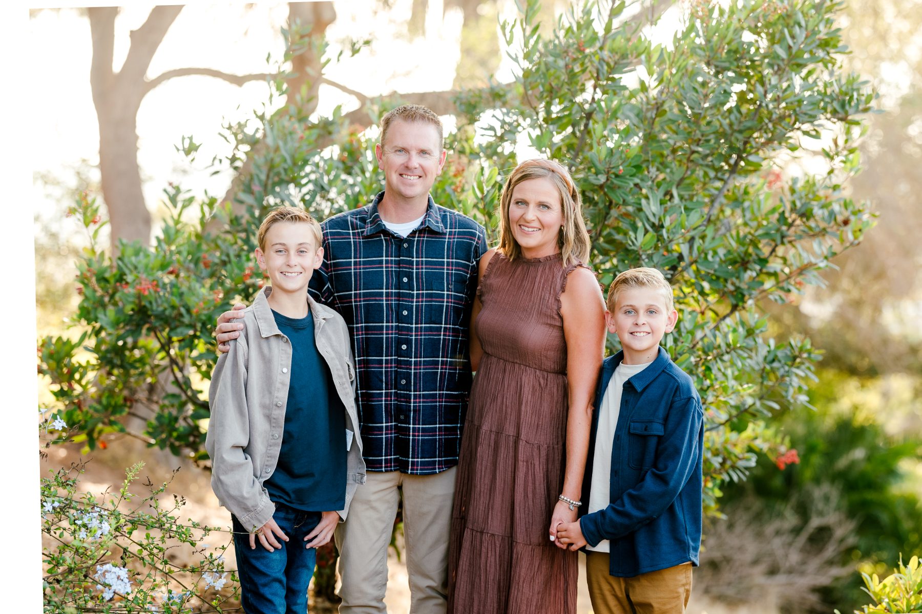 Parents and sons hug beneath greenery in a garden setting