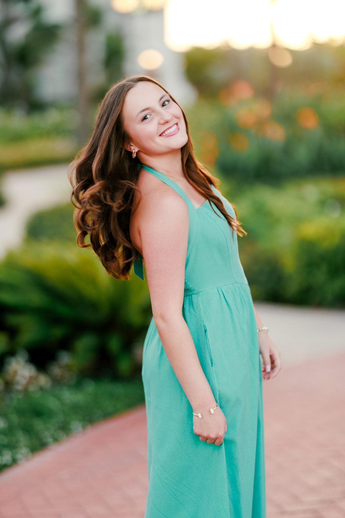 Woman in teal dress twirls on garden path at Hotel Del Coronado