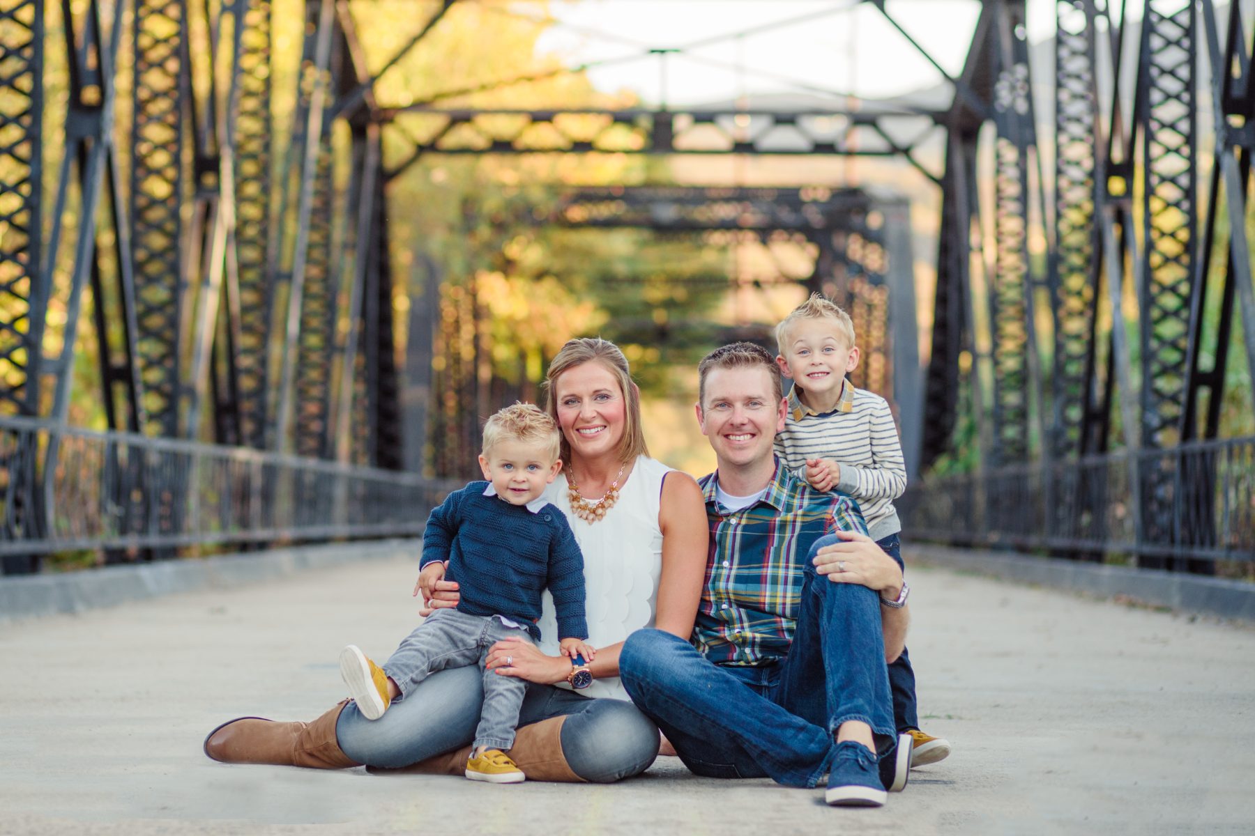 Family sits together on an old iron truss bridge in autumn light