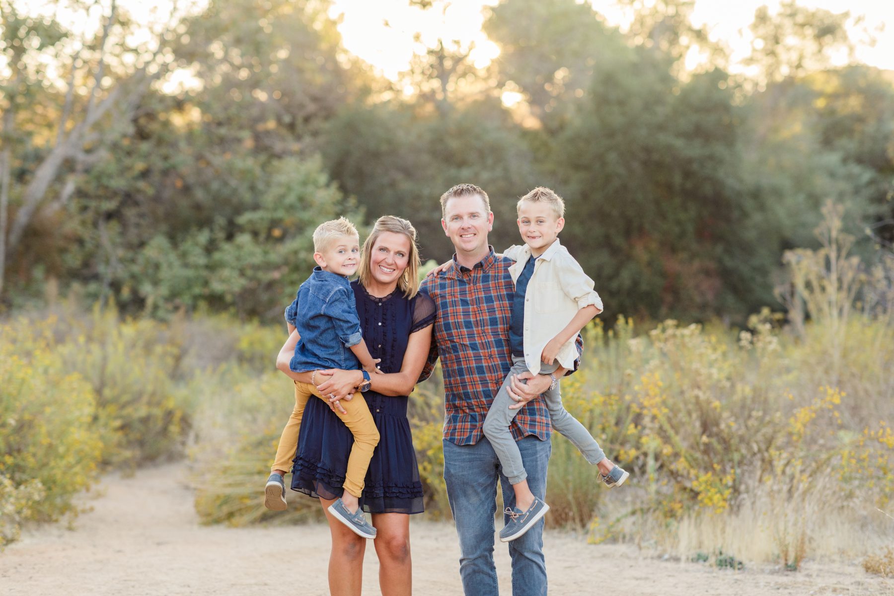 Parents lift two young sons while standing in golden brushland at sunset