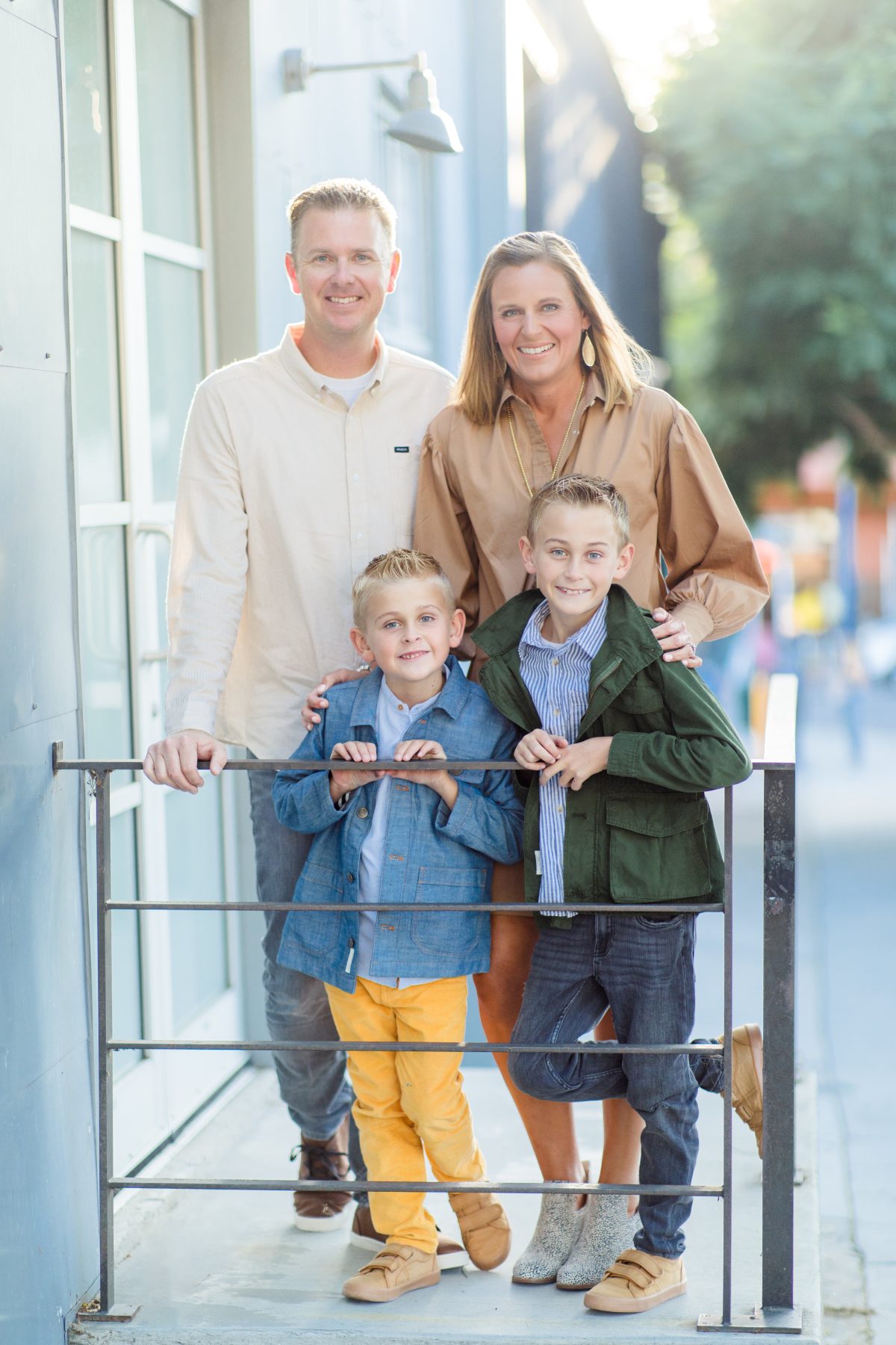 Family of four stands together near metal railing on city sidewalk