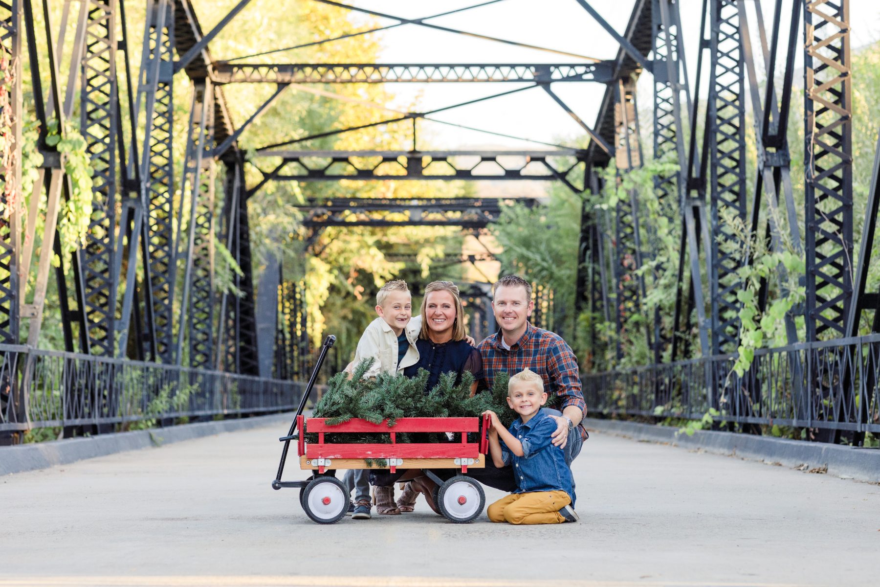 Family gathers around red wagon filled with greenery on iron bridge