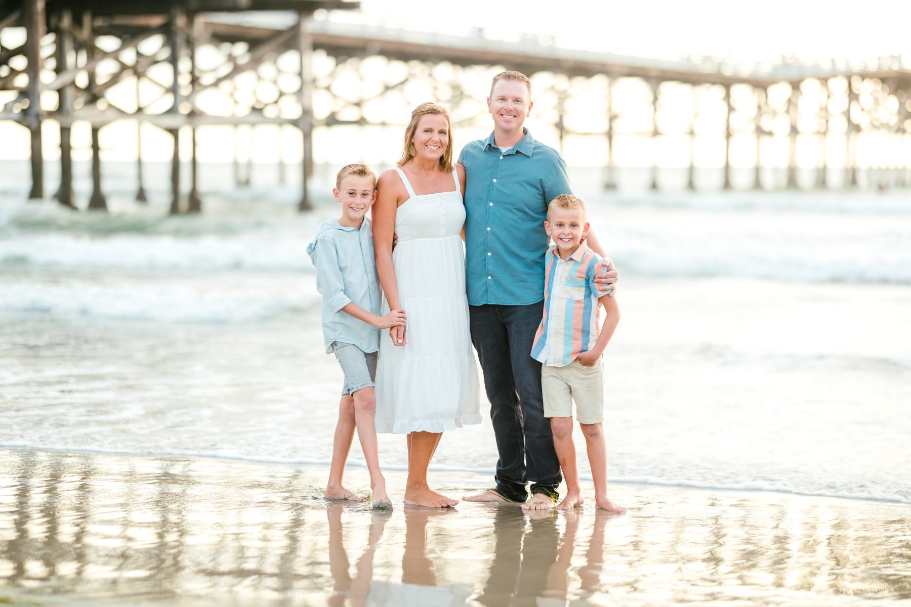 Family of four stands ankle-deep in waves near a San Diego pier