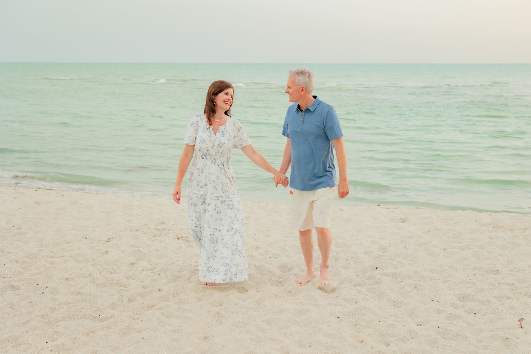 Couple holds hands walking along the shore at Sanibel Island