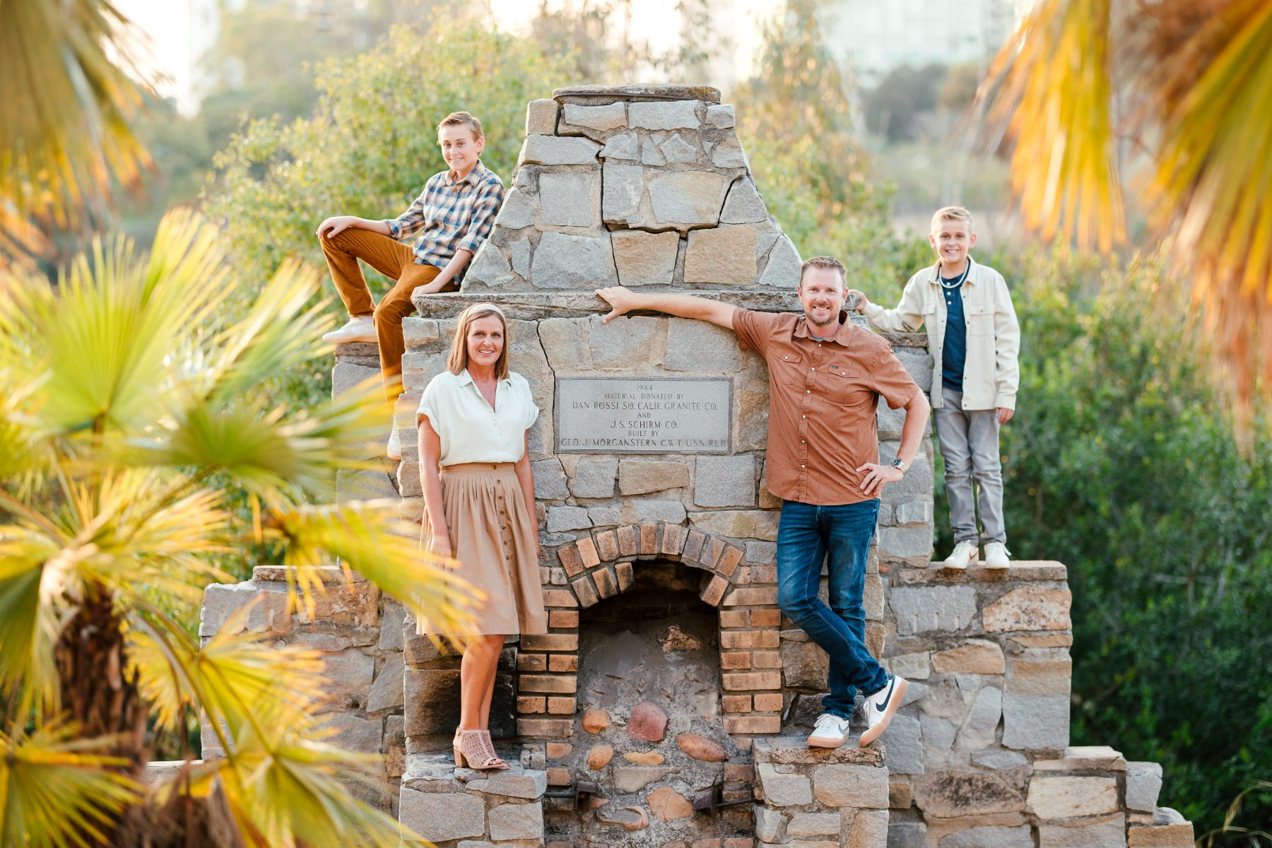 Family poses on a stone fireplace ruin surrounded by palm trees