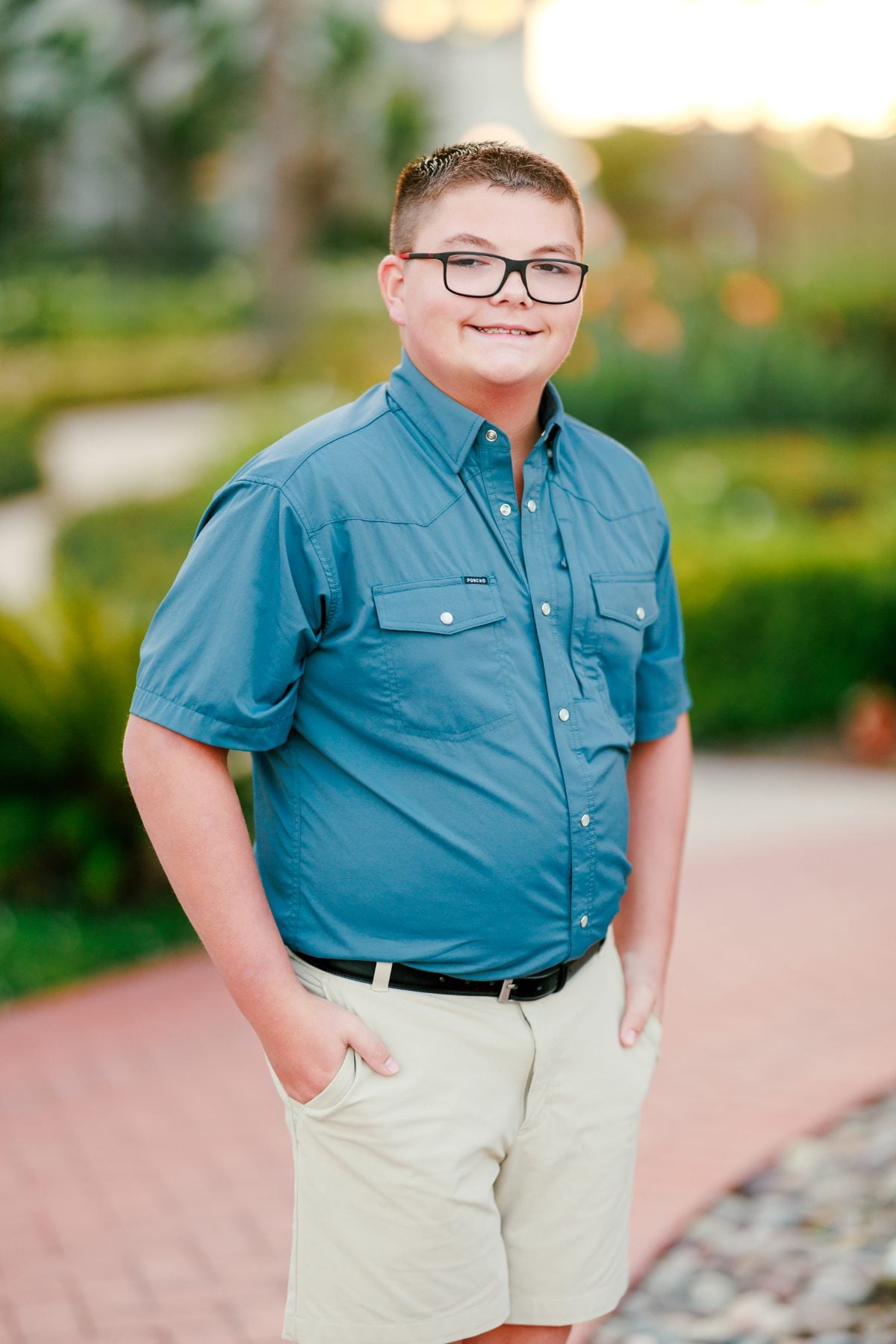 Teen boy in blue shirt and khaki shorts stands for solo portrait