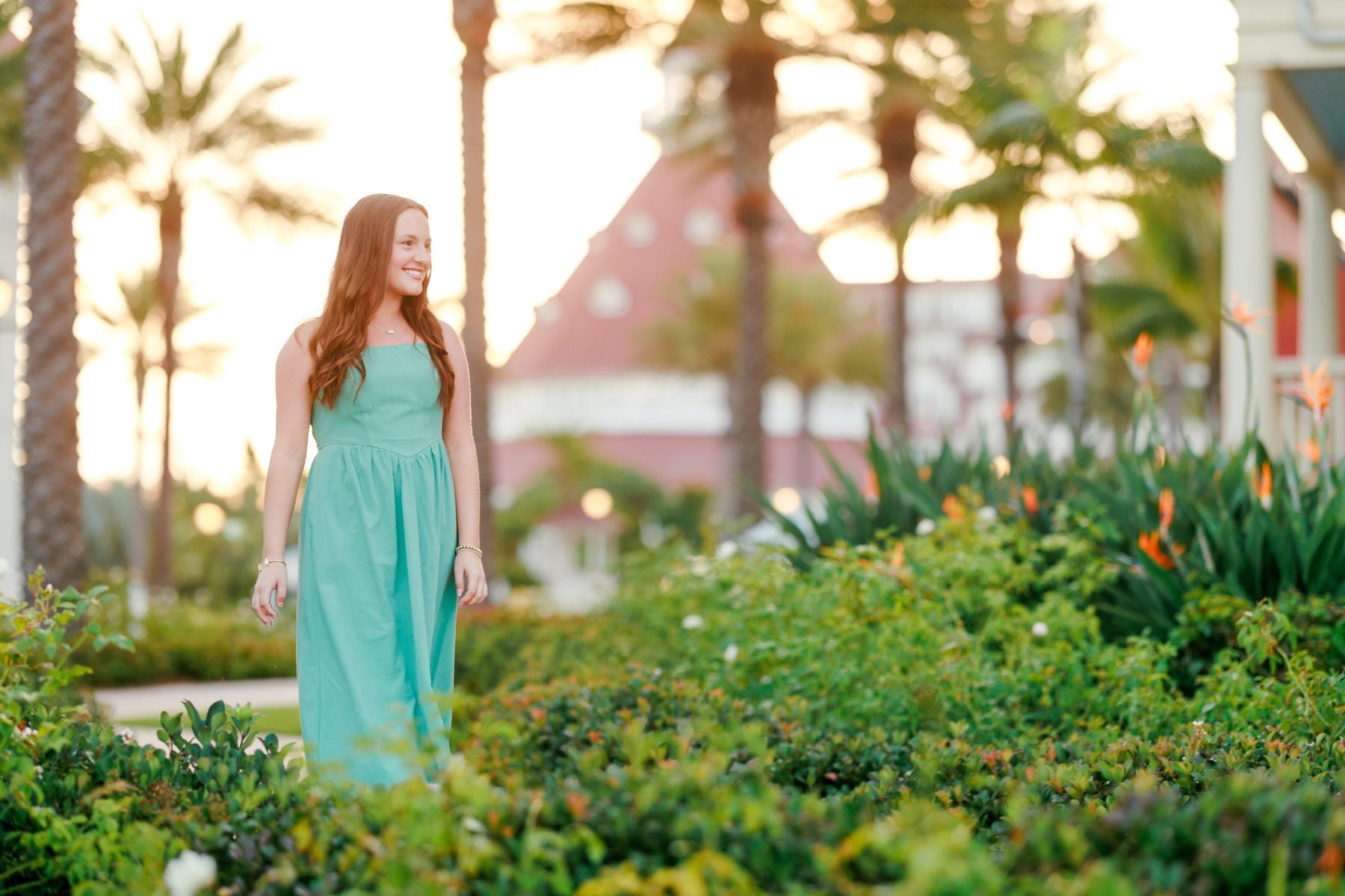 Teen girl in teal dress stands among palms near Hotel del Coronado