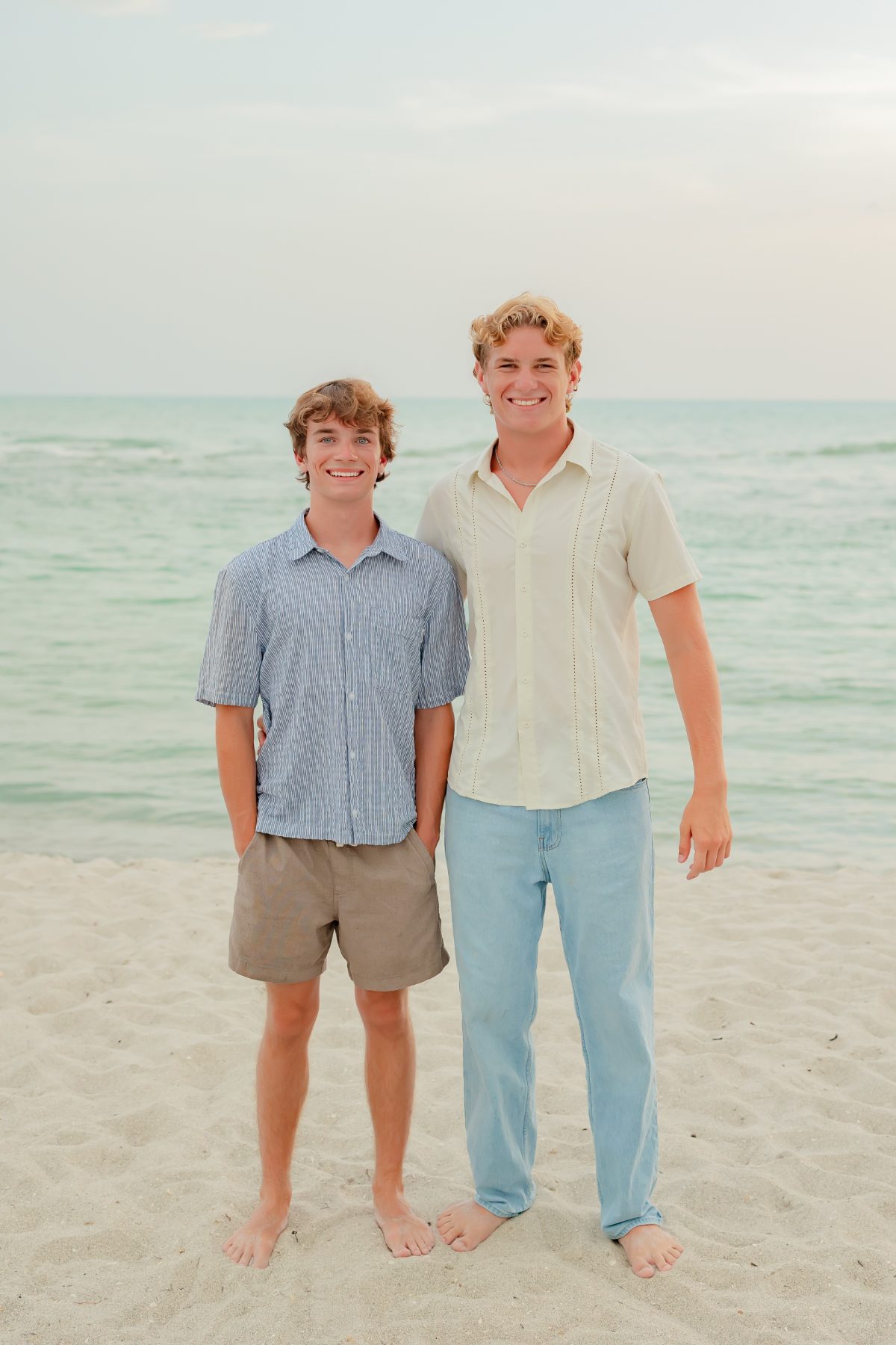 Two teenage brothers stand side by side near the ocean waves