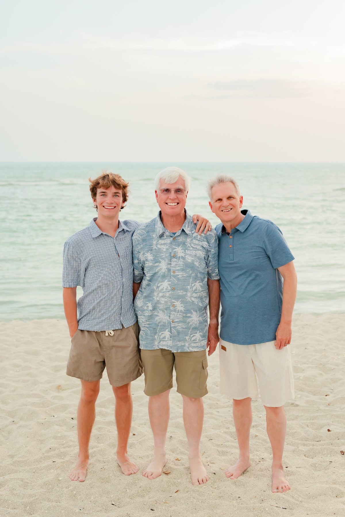 Three generations of men stand together on the sandy beach