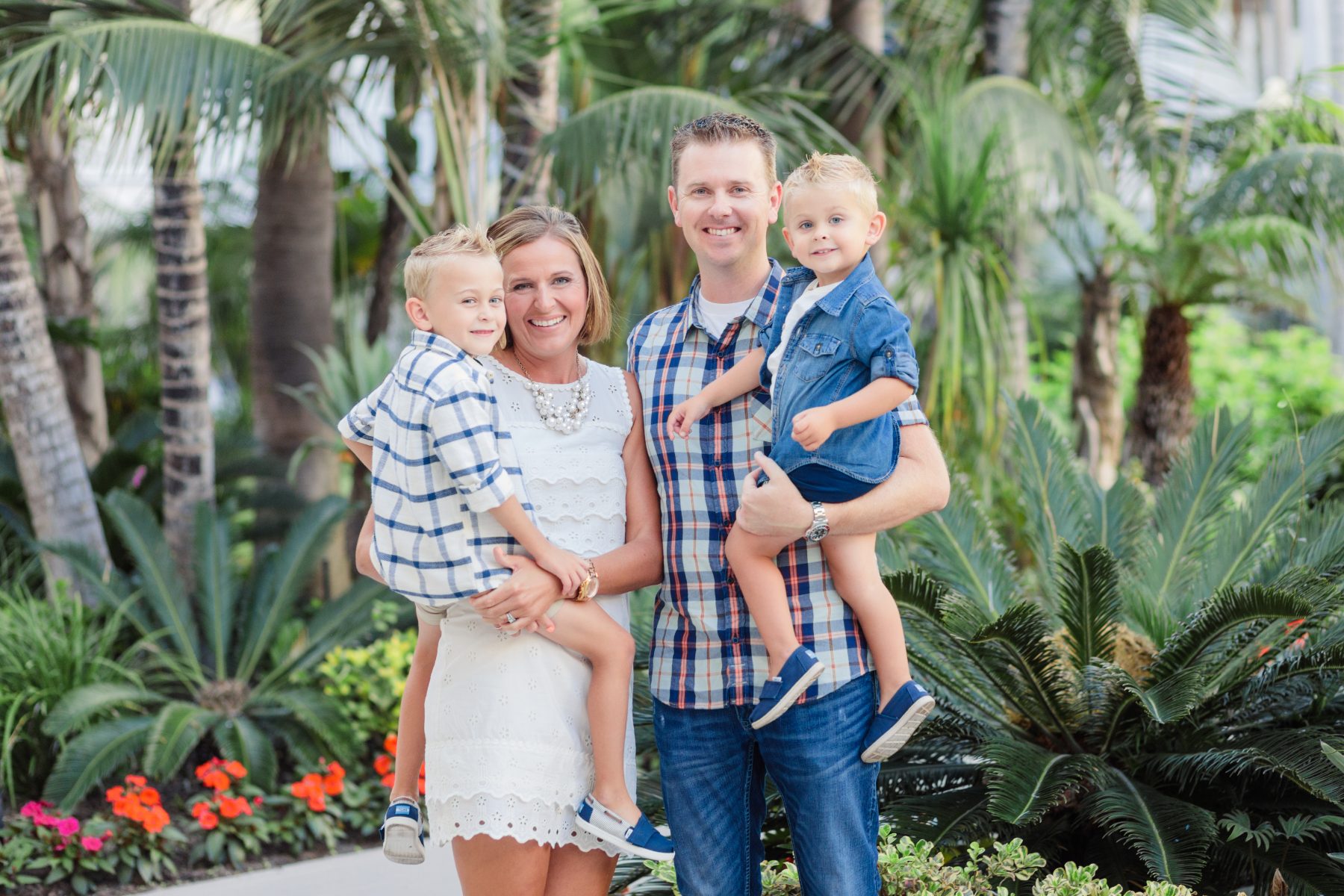 Family of four smiles among tropical palms, mom in white dress