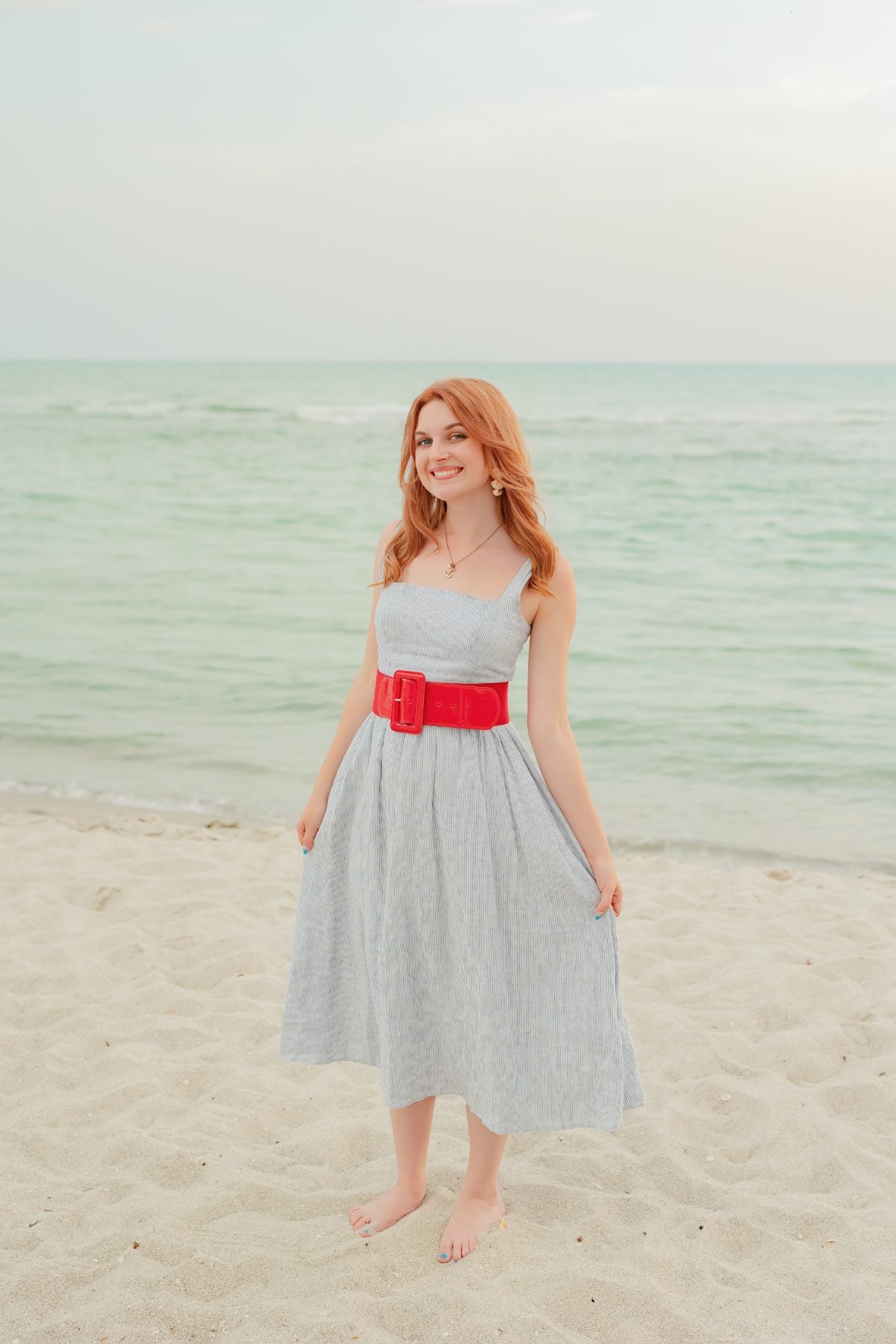 Young woman in striped dress with red belt stands on the beach