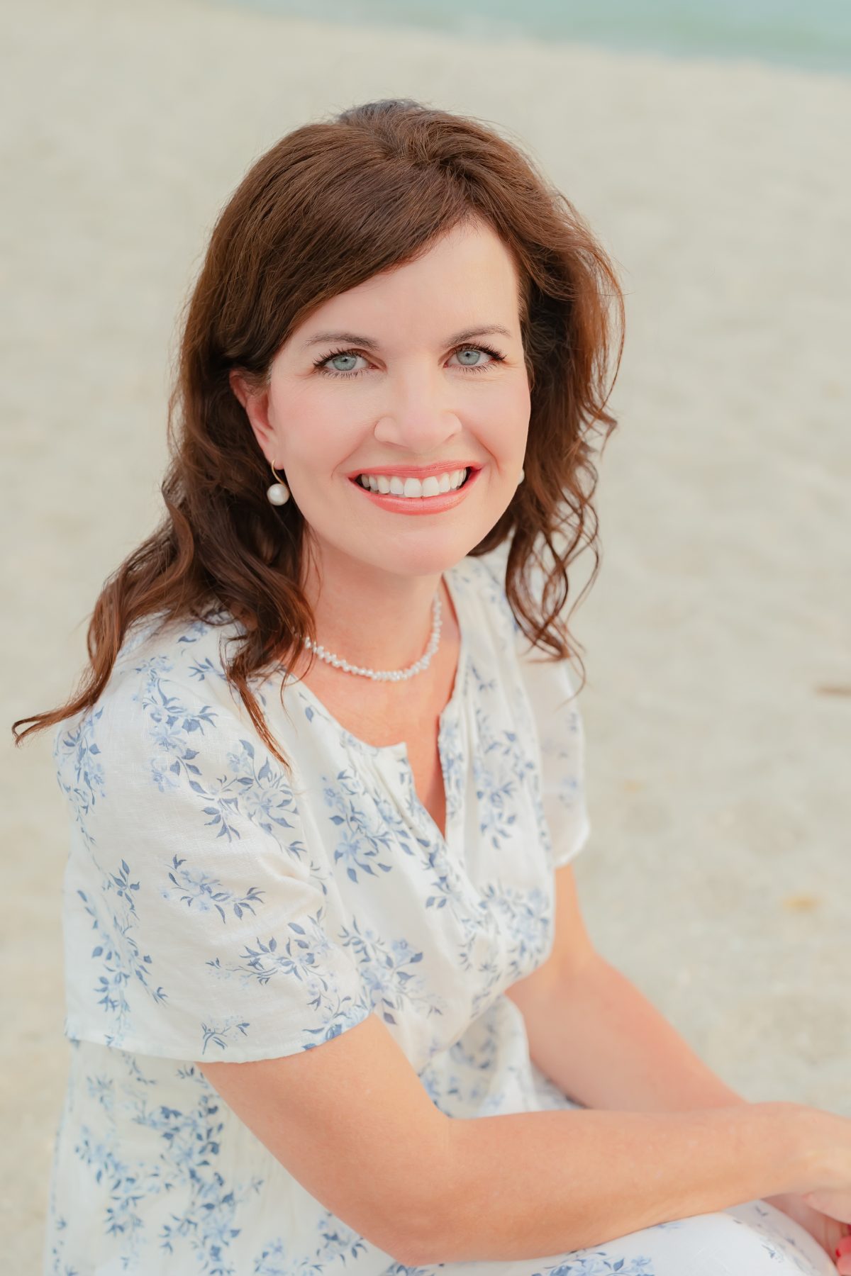 Woman in floral dress smiles for a seated beach portrait