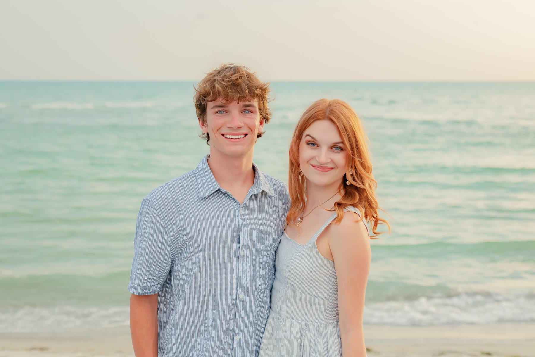 Curly-haired young man and redhead woman smile together by the ocean