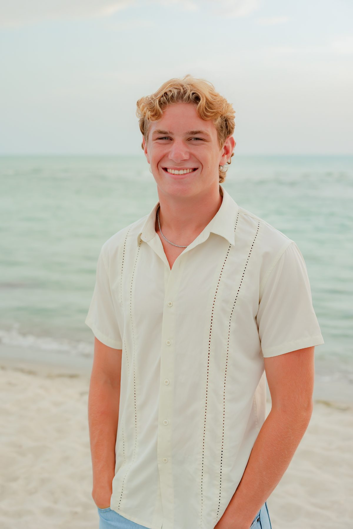 Young man in cream shirt smiles on the sandy Sanibel shore