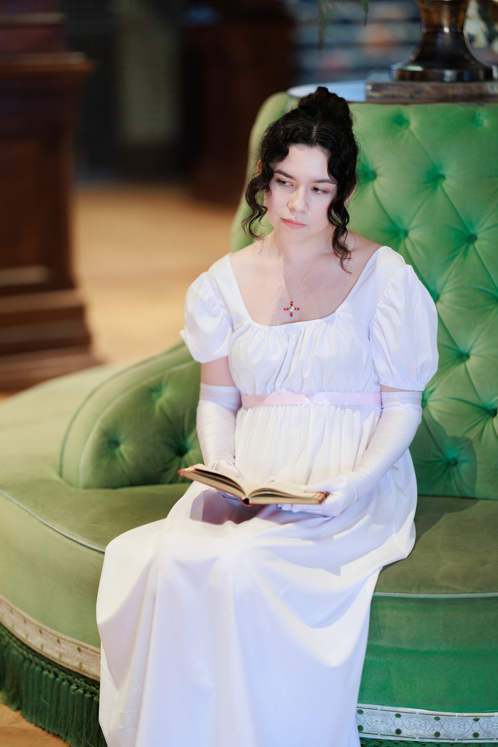 Amanda Fagan’s Love, Jane — 05 Woman in white dress reading open book while seated on green velvet chair