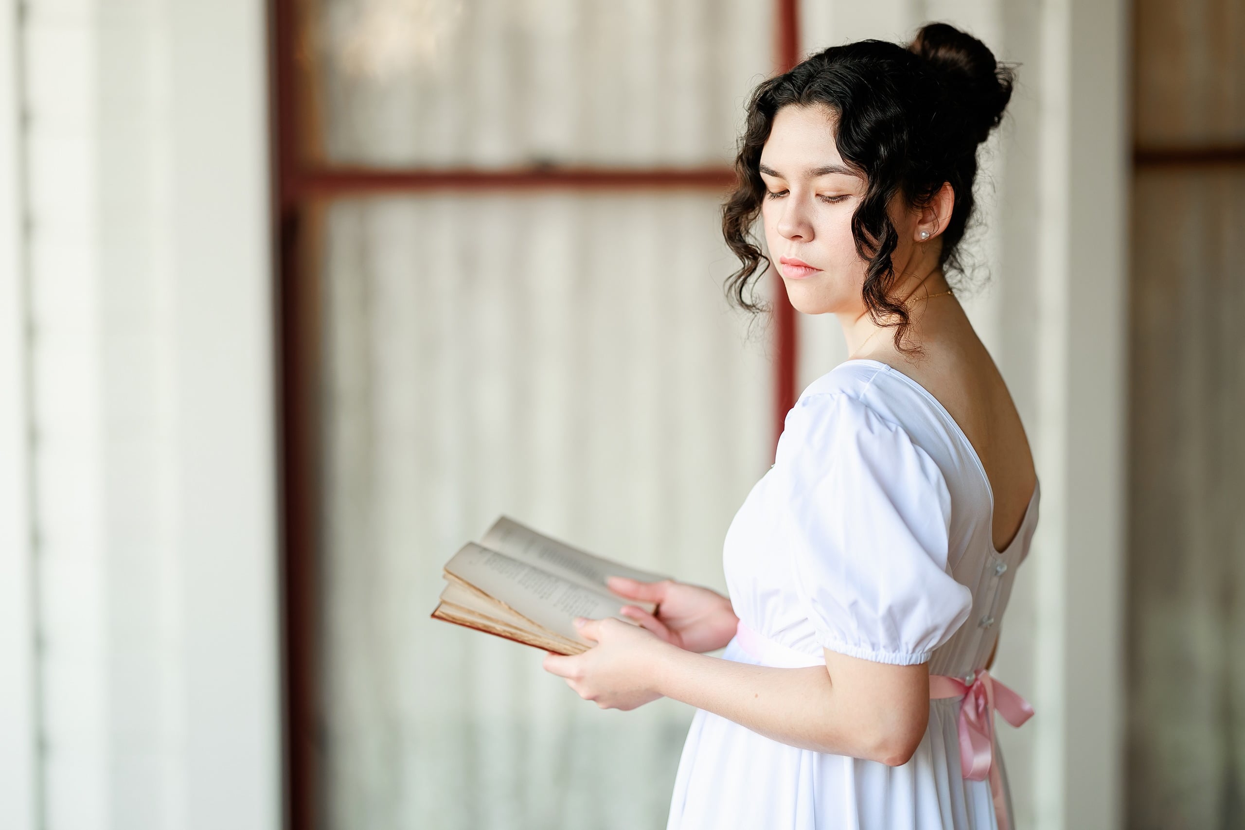 Amanda Fagan’s Love, Jane — 08 Woman in white dress holding open book, looking down pensively near columns