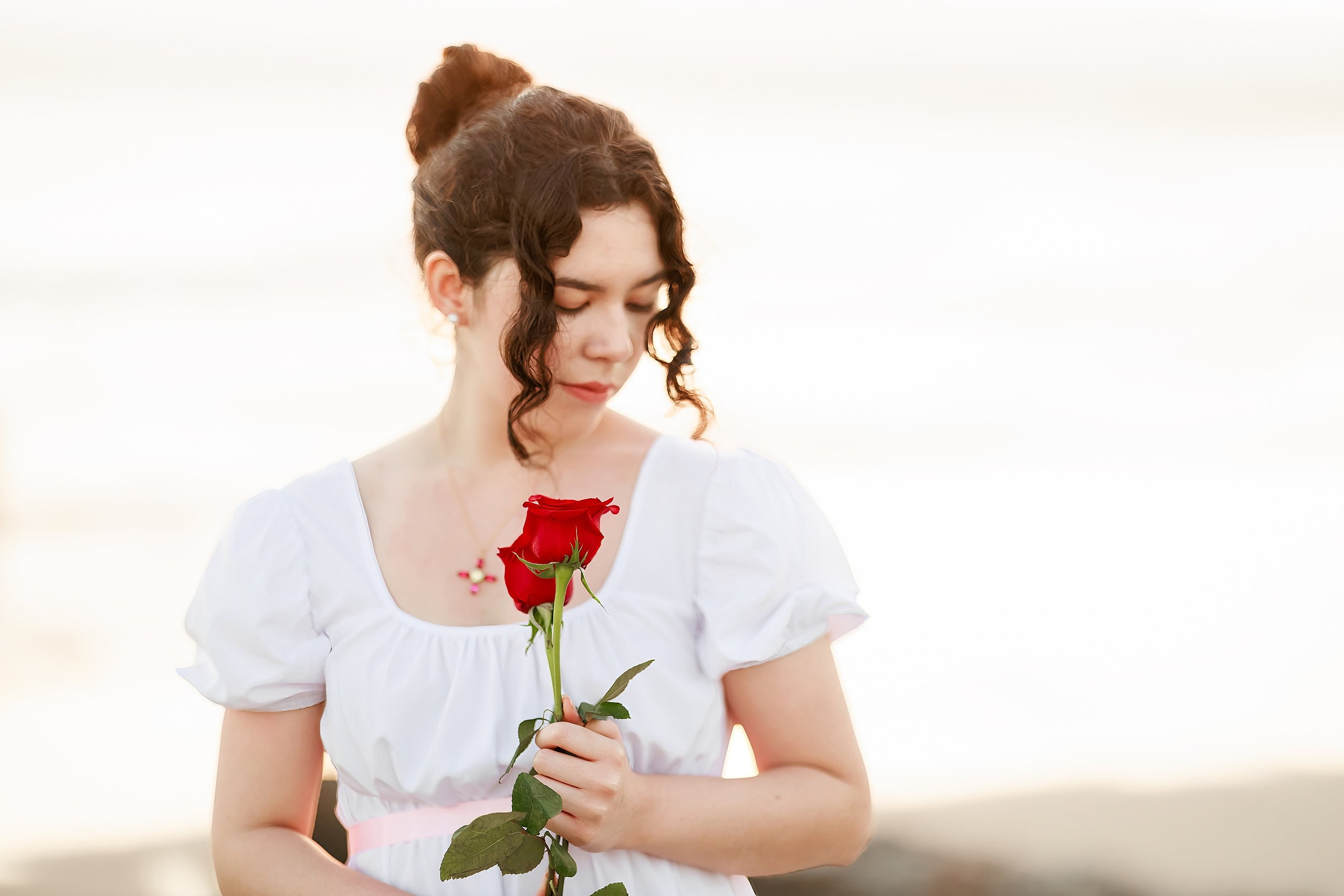 Amanda Fagan’s Love, Jane — 17 Woman in white dress holding red rose on beach, looking down pensively