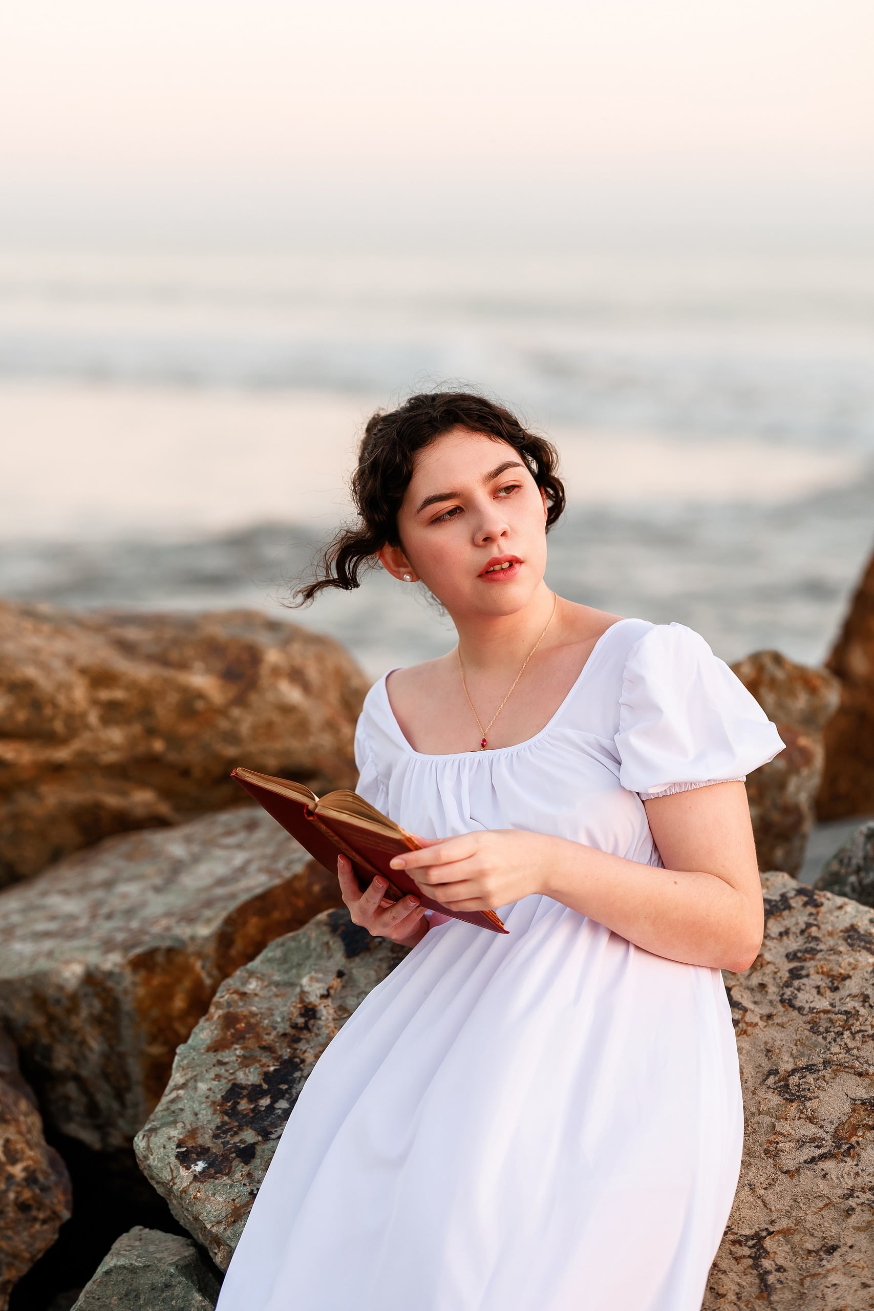 Amanda Fagan’s Love, Jane — 22 Woman in white dress holding red rose on beach, gazing over rocky shoreline