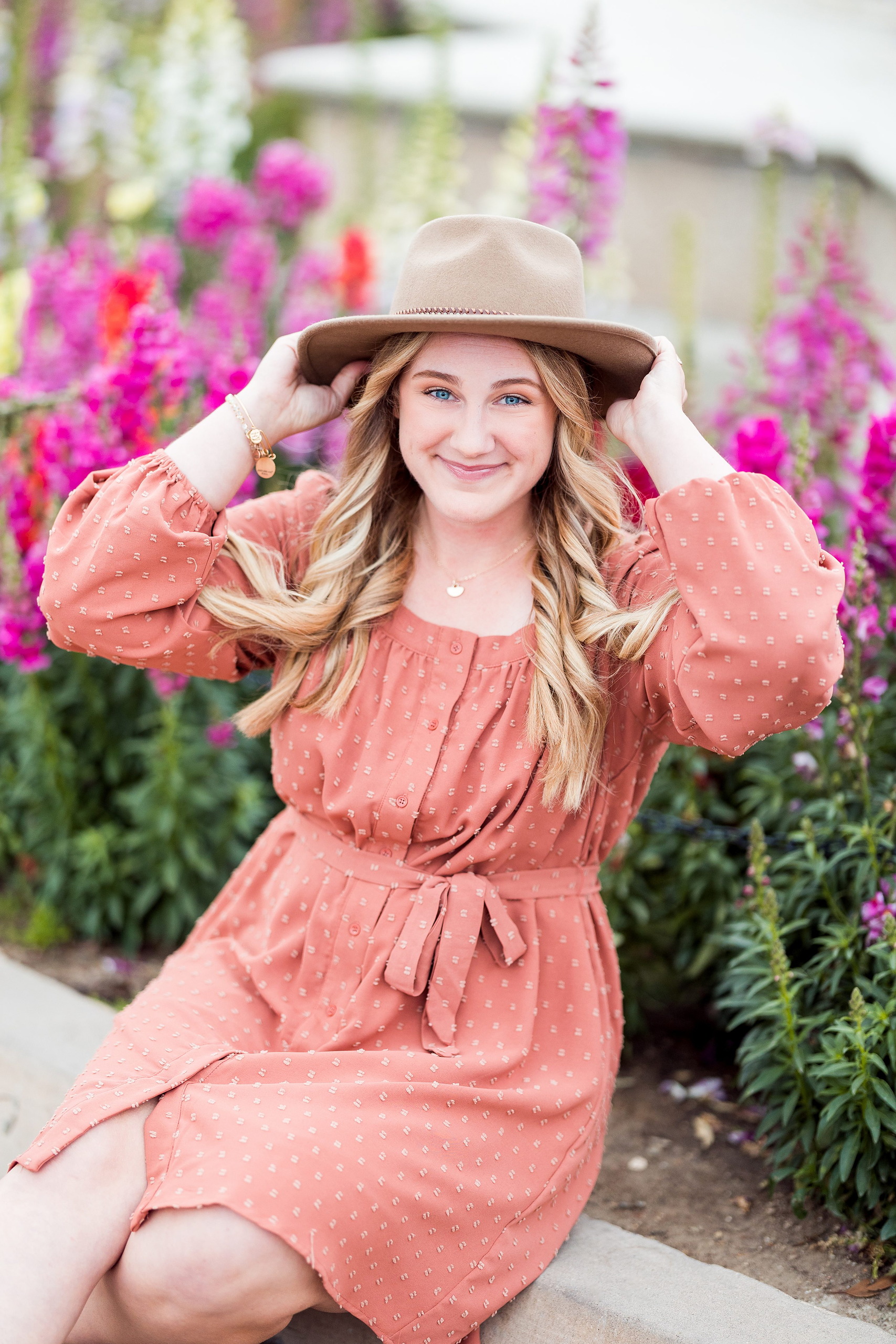 Balboa Park Senior Photography Session — 01 Senior in pink dress with puffed sleeves holding tan hat among vivid magenta flowers