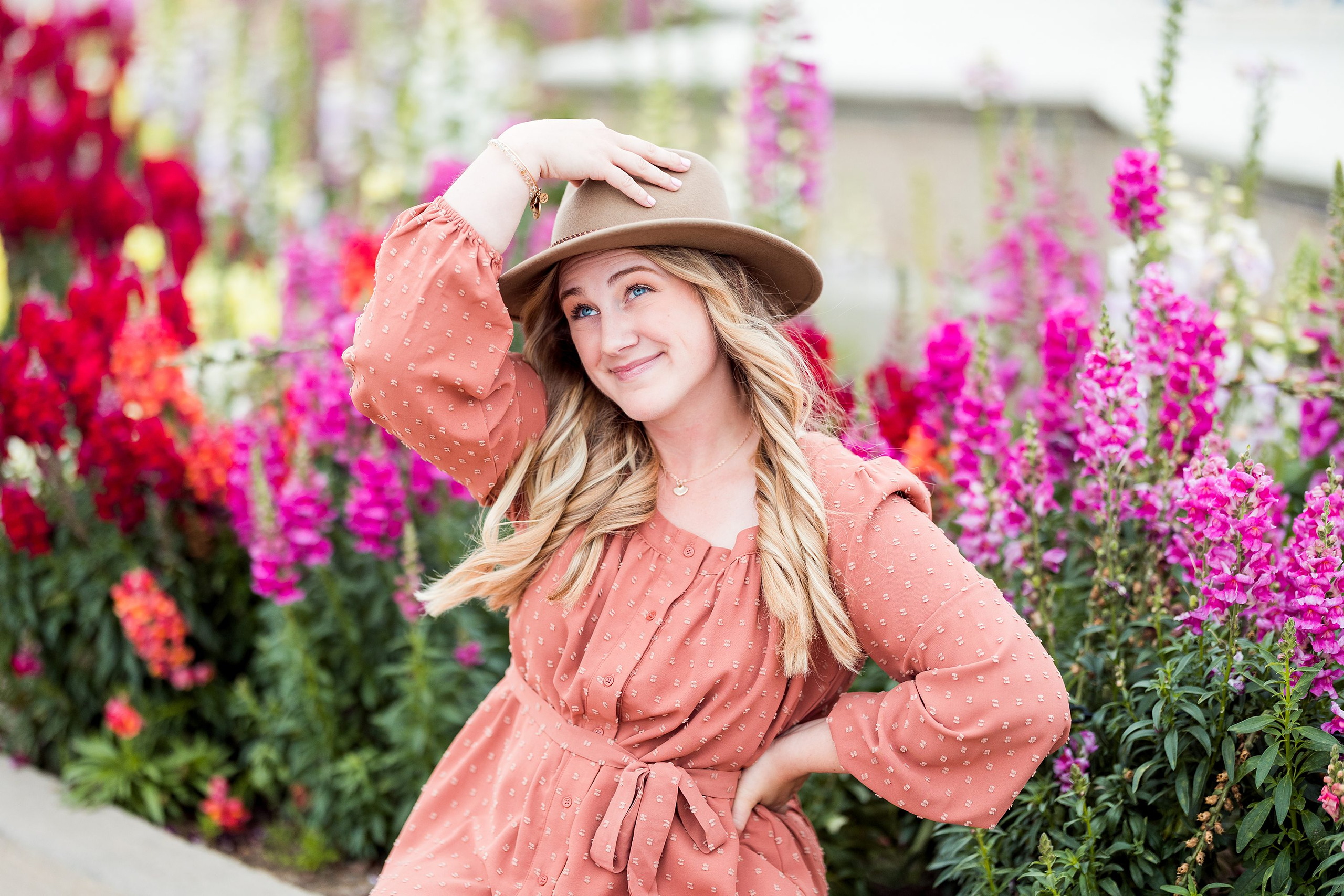 Balboa Park Senior Photography Session — 03 Senior in pink dress hand on hat brim, surrounded by pink and red blooms