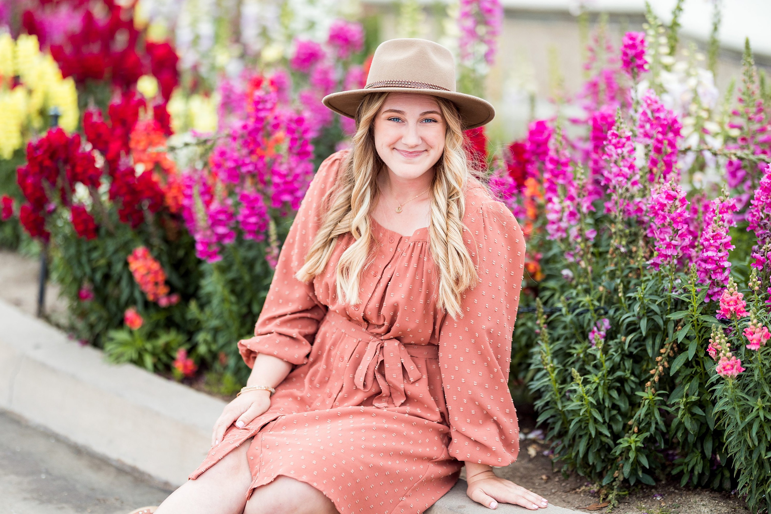 Balboa Park Senior Photography Session — 06 Senior sitting among bright magenta flowers wearing coral dress and tan hat