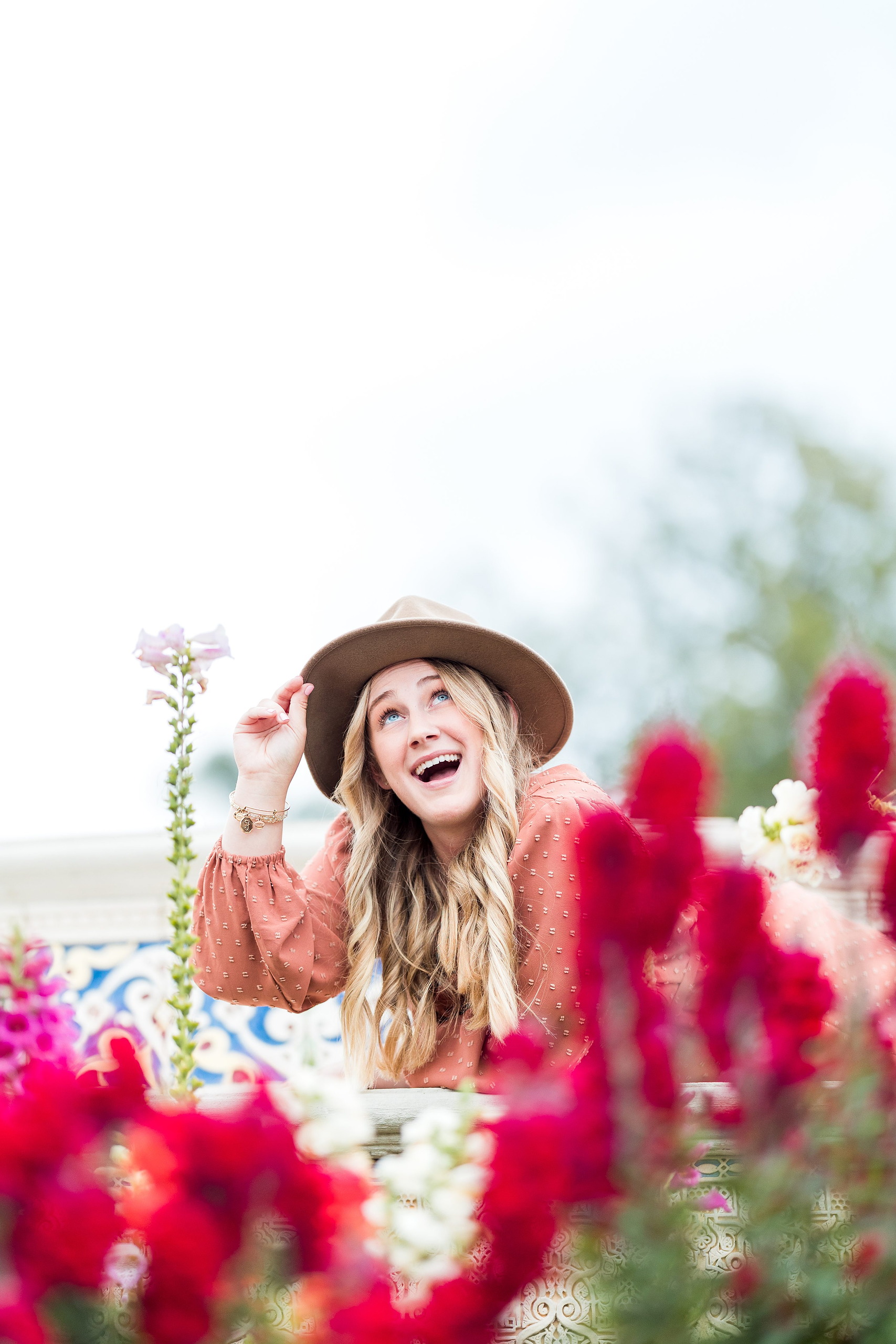 Balboa Park Senior Photography Session — 09 Senior in pink dress with hand on hat brim standing among red flowers at Balboa Park