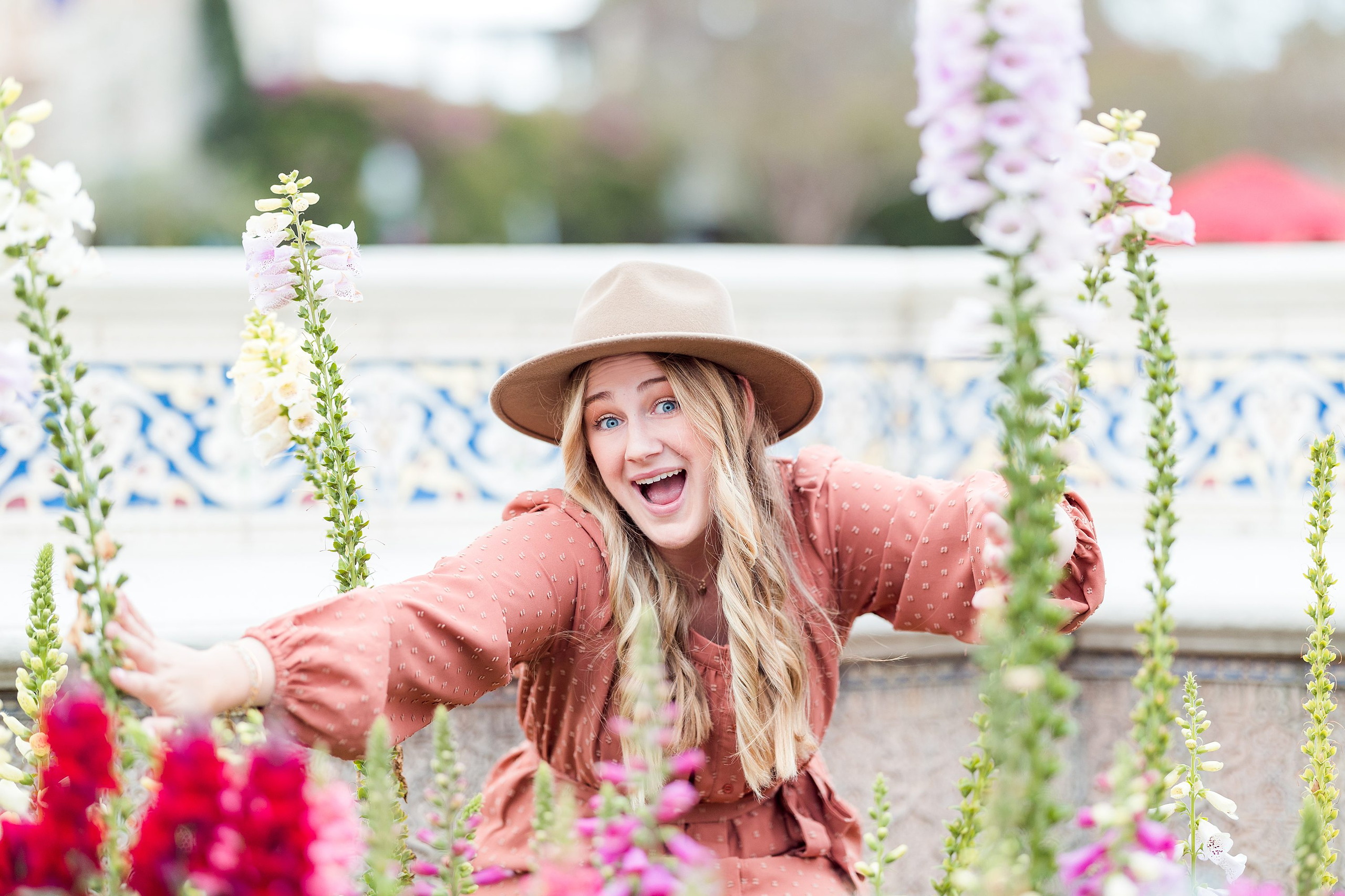 Balboa Park Senior Photography Session — 10 Senior standing at water's edge with arms out, pink dress, flowering plants in foreground